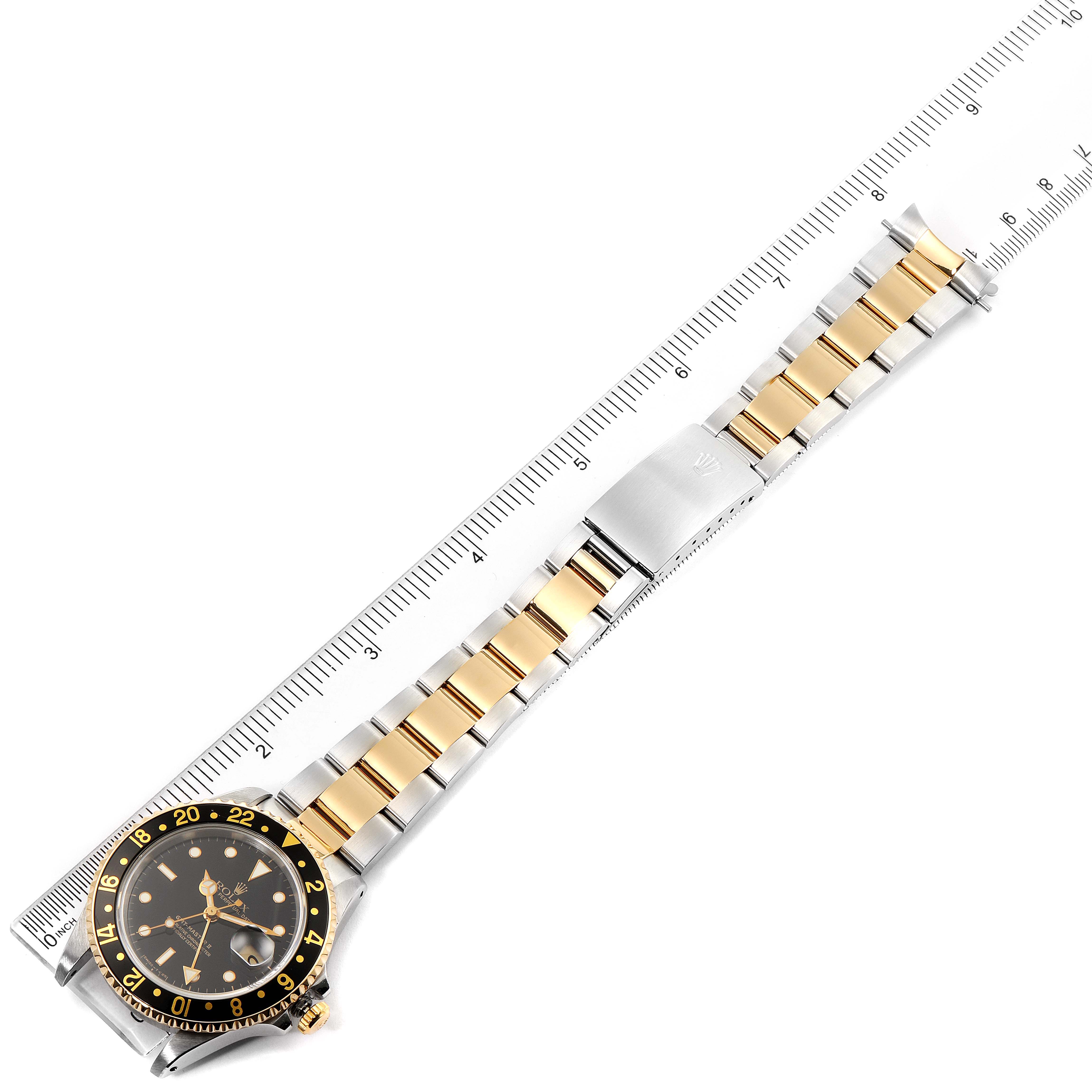 The image shows a Rolex GMT-Master 16713 Men's Steel and Gold (two tone) Black Dial 16713 Men's Steel and Gold (two tone) Black Dial watch laid horizontally with its full bracelet and a ruler for scale.