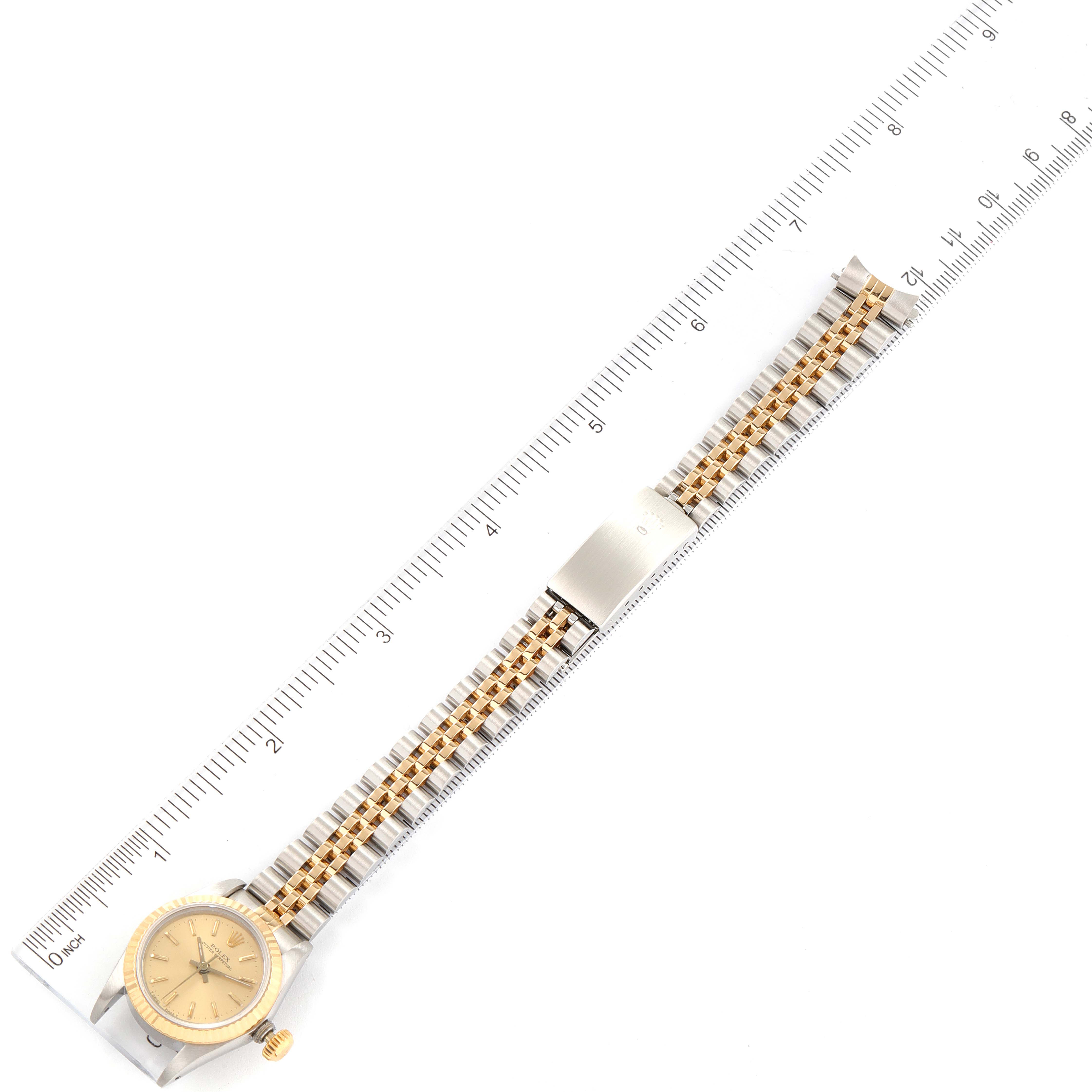 The image shows a Rolex Oyster Perpetual 67193 Women
s Steel and Gold (two tone) Champagne Dial 67193 Women
s Steel and Gold (two tone) Champagne Dial watch laid flat, aligned next to a measuring ruler, displaying the watch face, crown, case, and band.