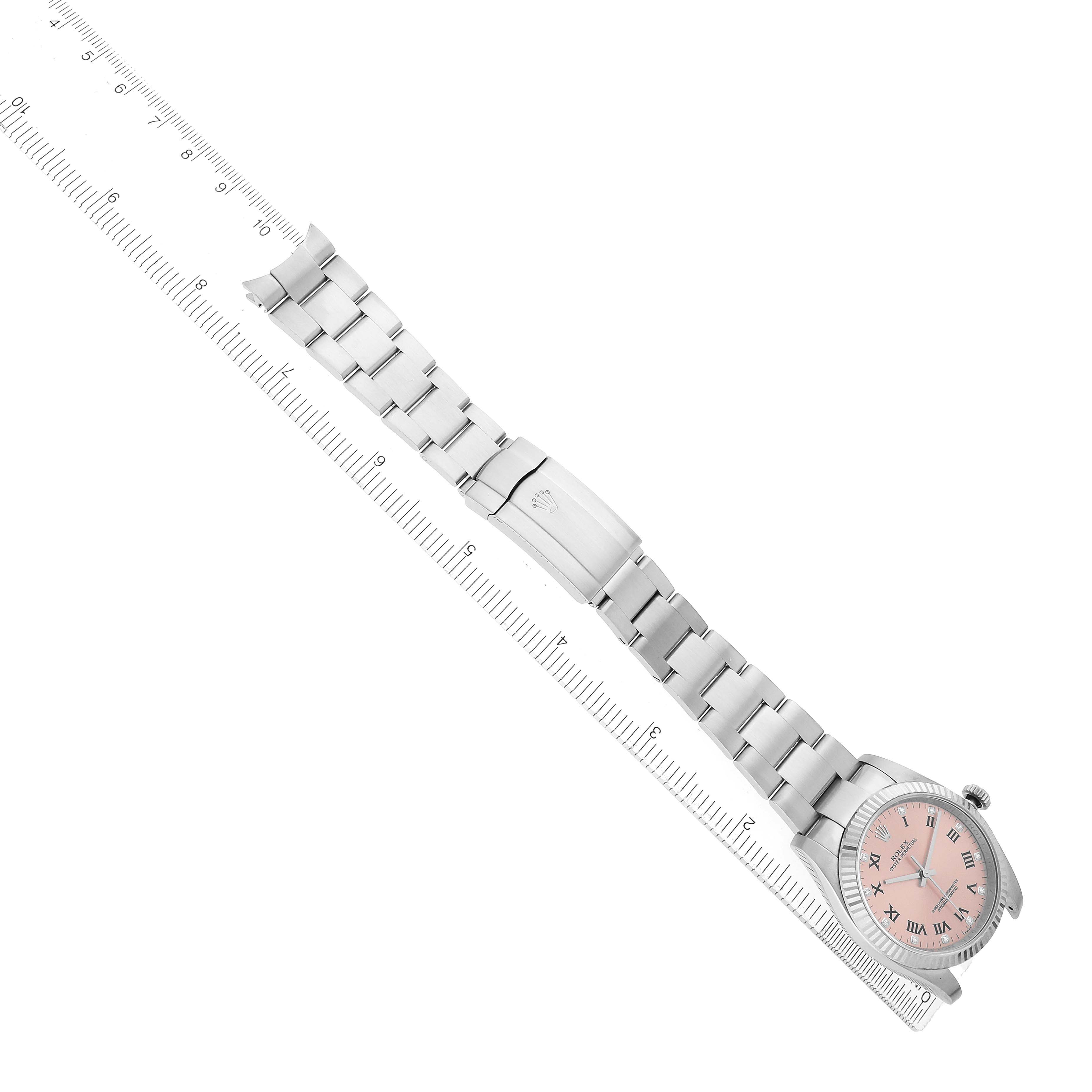 The Rolex Oyster Perpetual 116034 Men's Stainless Steel Pink Dial watch is shown from a top view, featuring its full bracelet and clasp, next to a ruler.