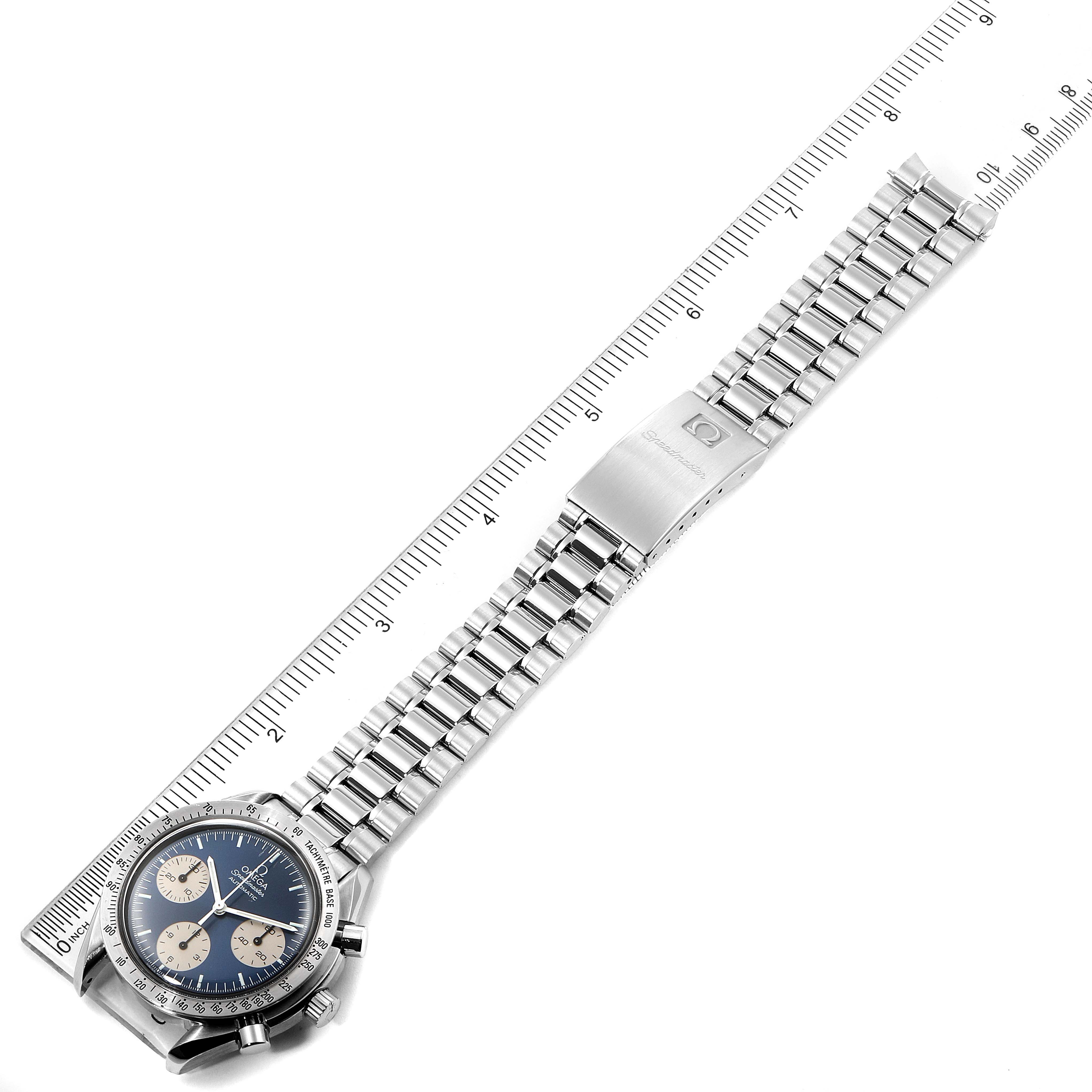 The Omega Speedmaster 3510.82.00 Men
s Stainless Steel Blue Dial 3510.82.00 Men
s Stainless Steel Blue Dial watch is shown from a diagonal top-down angle, displaying the entire watch and its metal bracelet alongside a ruler.
