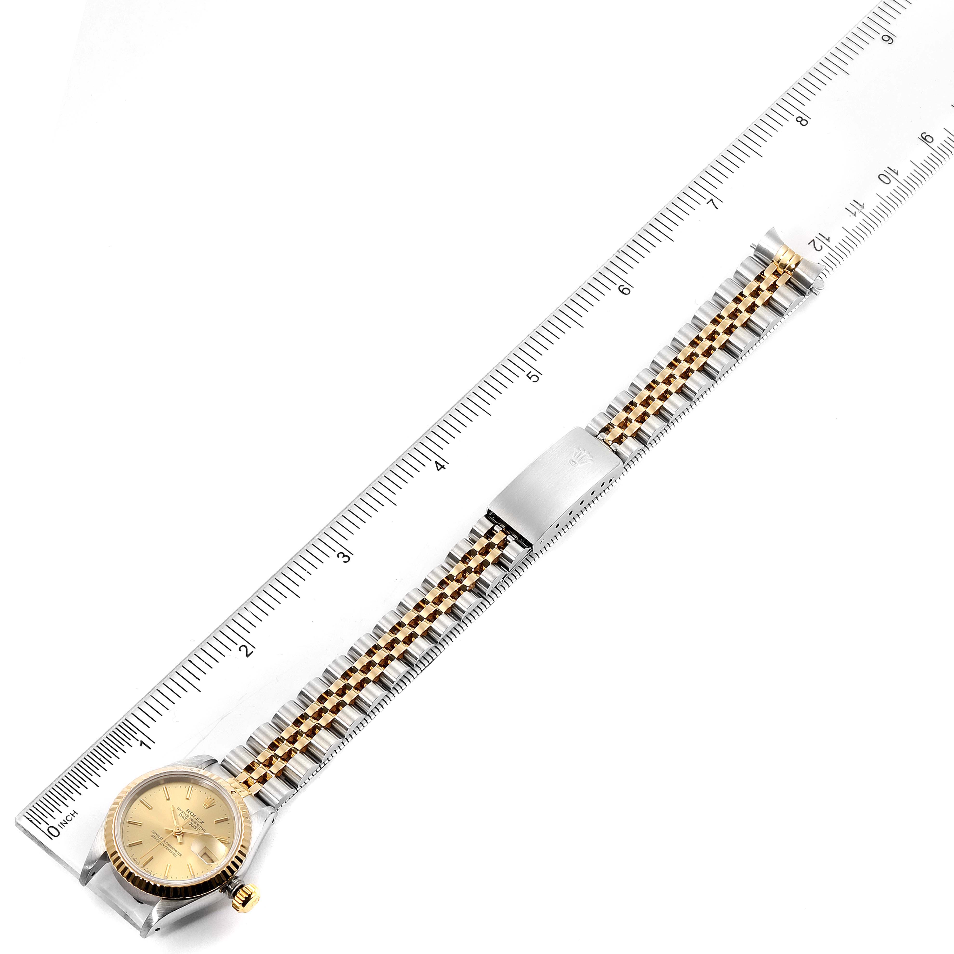 The image shows a side angle of a Rolex Datejust 69173 Women
s Steel and Gold (two tone) Champagne Dial 69173 Women
s Steel and Gold (two tone) Champagne Dial watch, with its whole band and clasp extended next to a ruler.