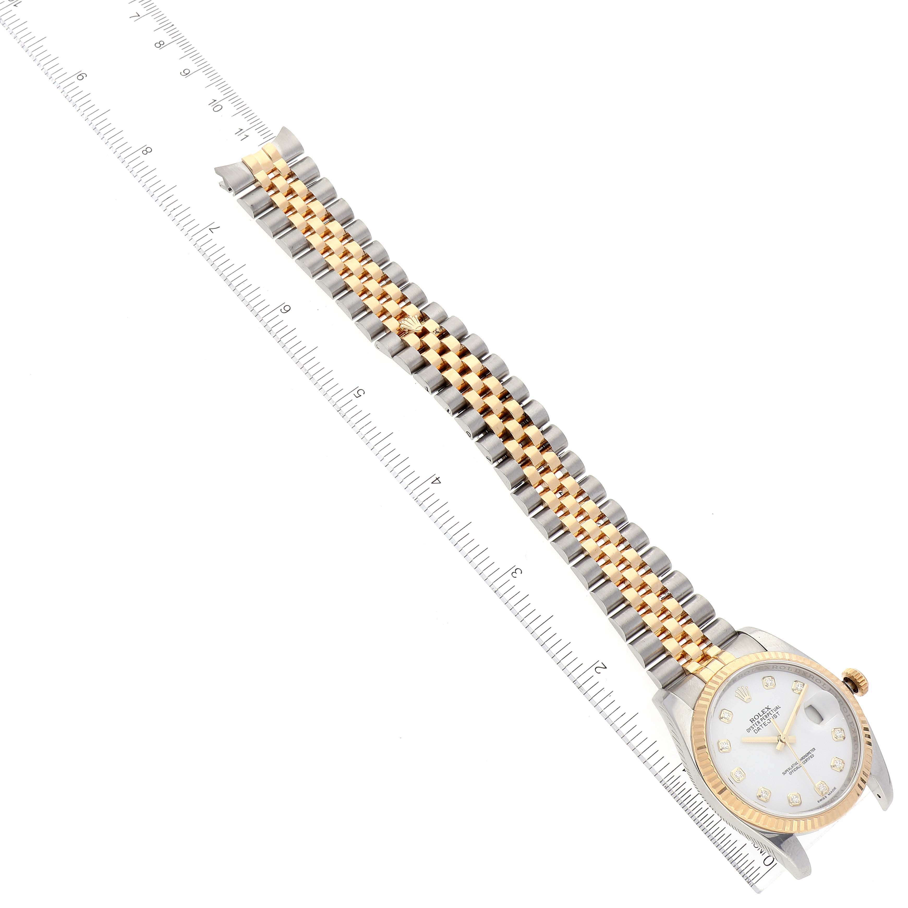 The image shows a Rolex Datejust 116233 Men's Steel and Gold (two tone) White Dial 116233 Men's Steel and Gold (two tone) White Dial watch from an angled top-down view, including its face, bezel, and two-tone bracelet, next to a ruler for scale.
