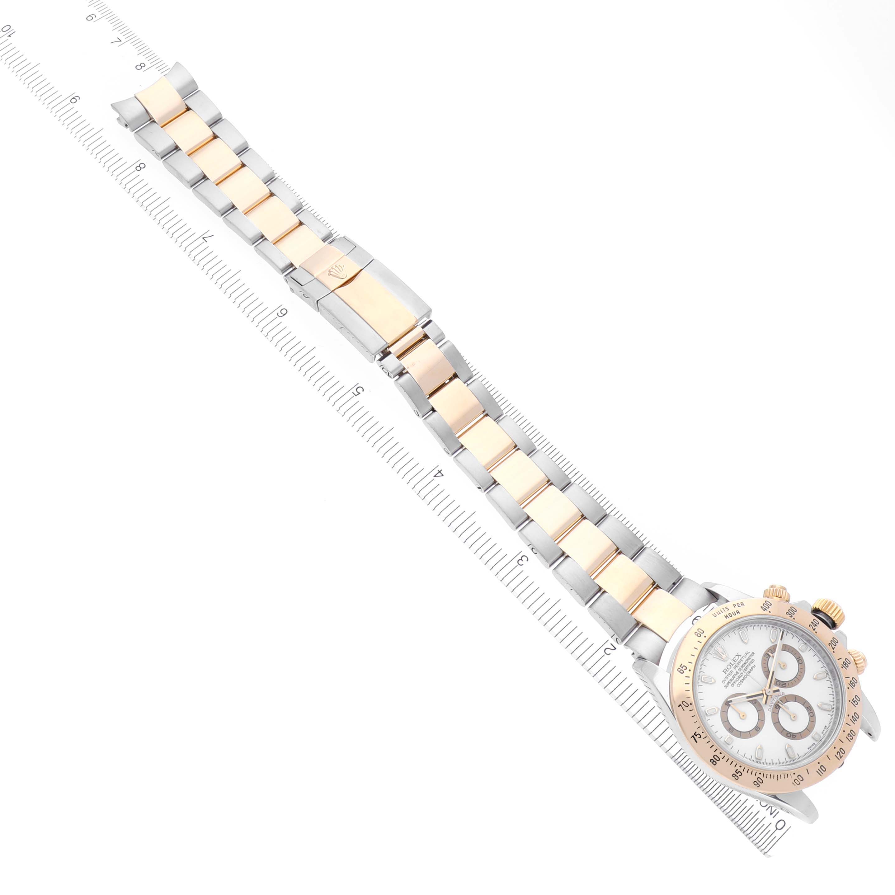The image shows the Rolex Daytona 116523 Men's Steel and Gold (two tone) White Dial 116523 Men's Steel and Gold (two tone) White Dial watch from a top-down angle, displaying its face and full bracelet laid alongside a ruler.