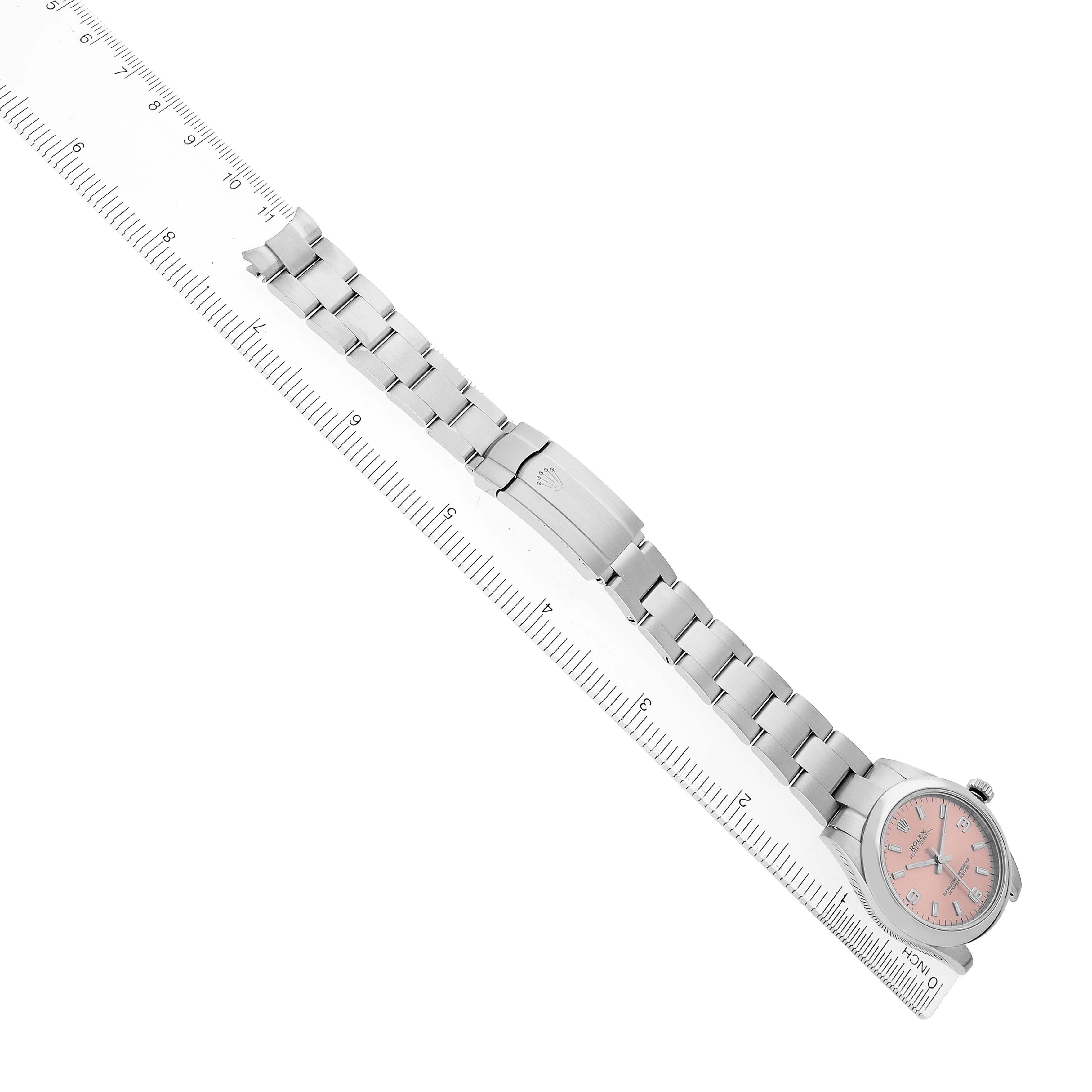 The Rolex Oyster Perpetual 177200 Women's Stainless Steel Pink Dial watch is shown fully extended at an angle, with the dial, bracelet, and clasp visible alongside a ruler.