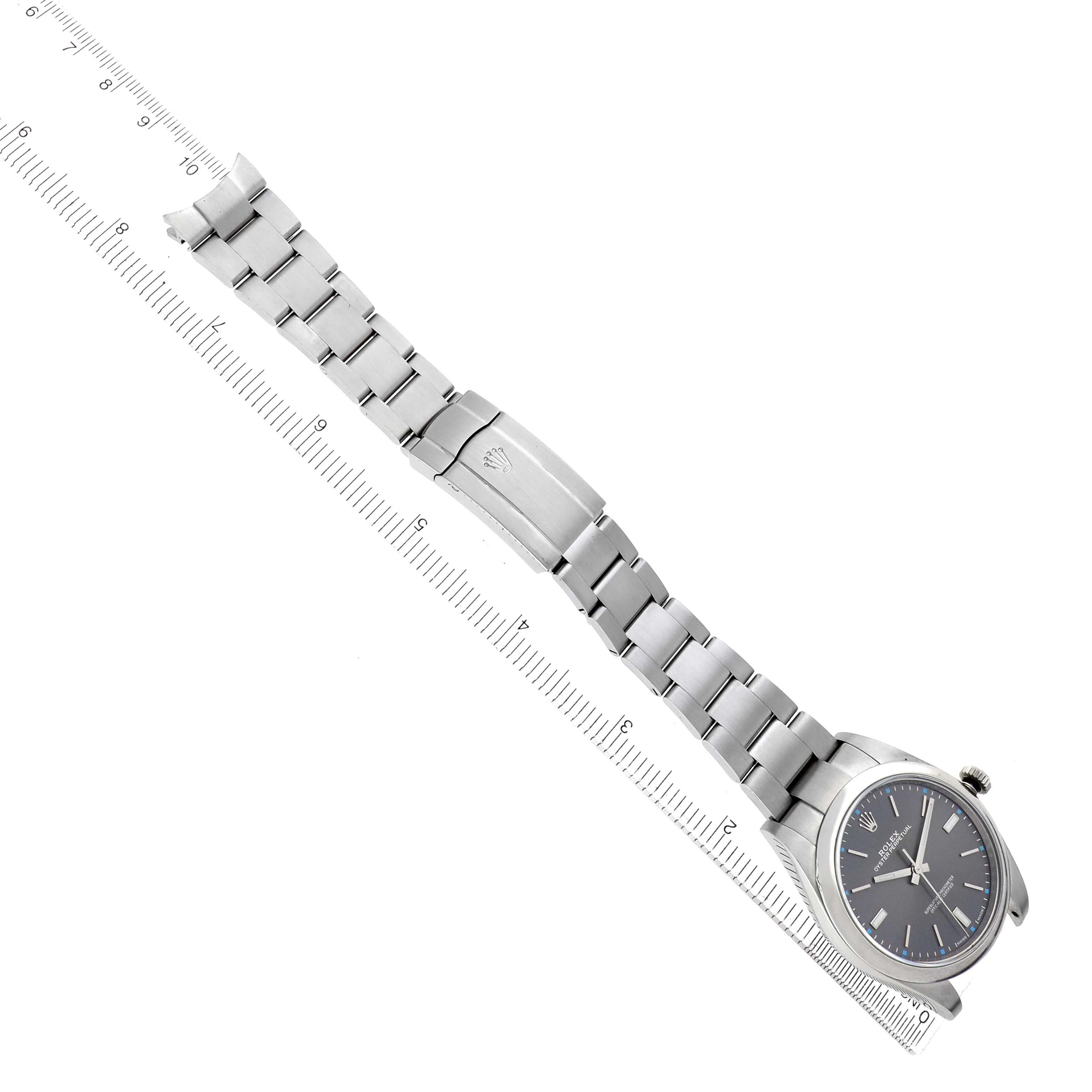 The Rolex Oyster Perpetual 114300 Men's Stainless Steel Silver Dial watch is shown from a top view, highlighting the dial, bracelet, and clasp next to a ruler.