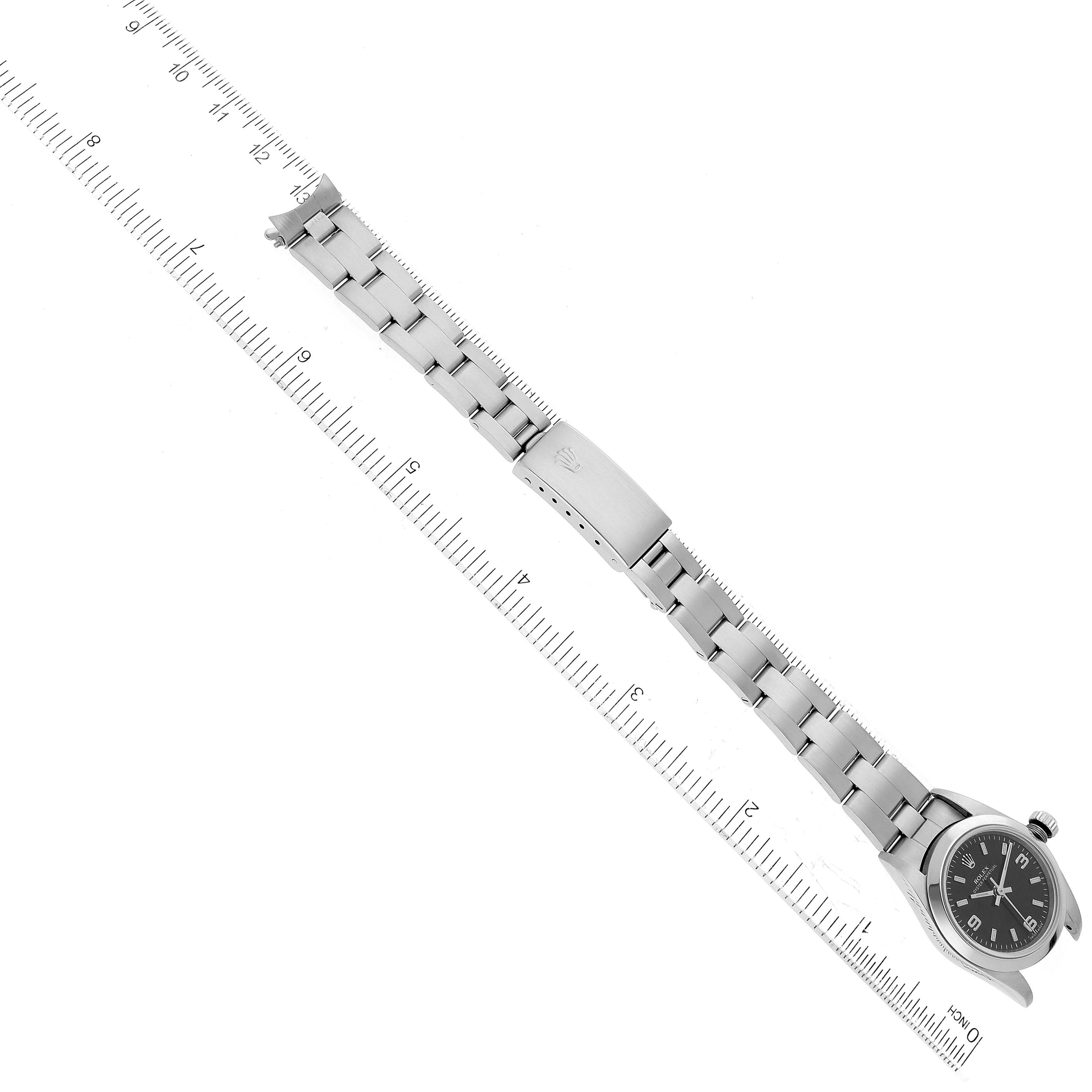 The image shows a top-down view of the Rolex Oyster Perpetual 76080 Women's Stainless Steel Black Dial 76080 Women's Stainless Steel Black Dial watch, displaying the face and bracelet alongside a ruler for scale.