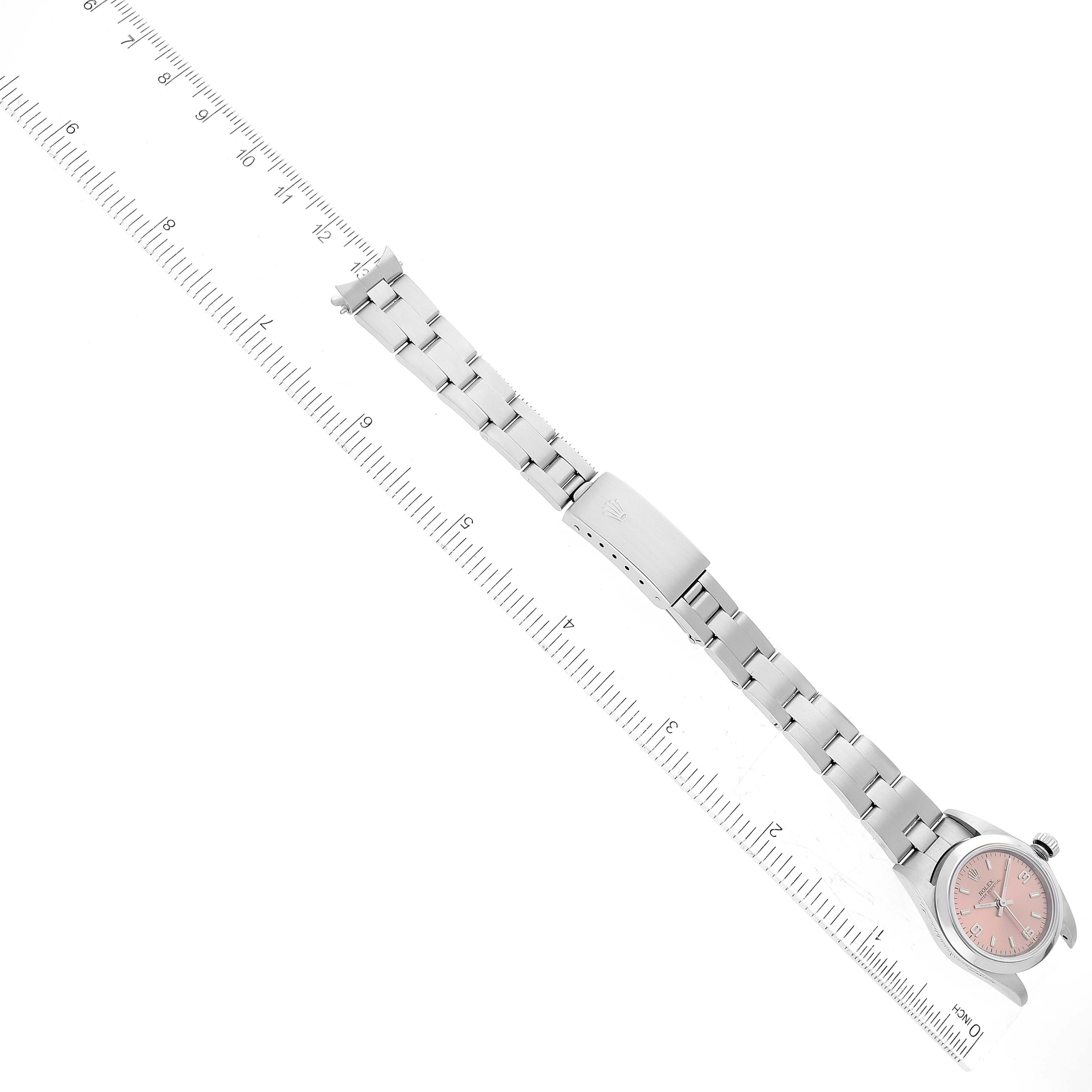 The Rolex Oyster Perpetual 76080 Women's Stainless Steel Orange Dial 76080 Women's Stainless Steel Orange Dial watch is shown fully extended next to a ruler, highlighting its bracelet and pink dial face.