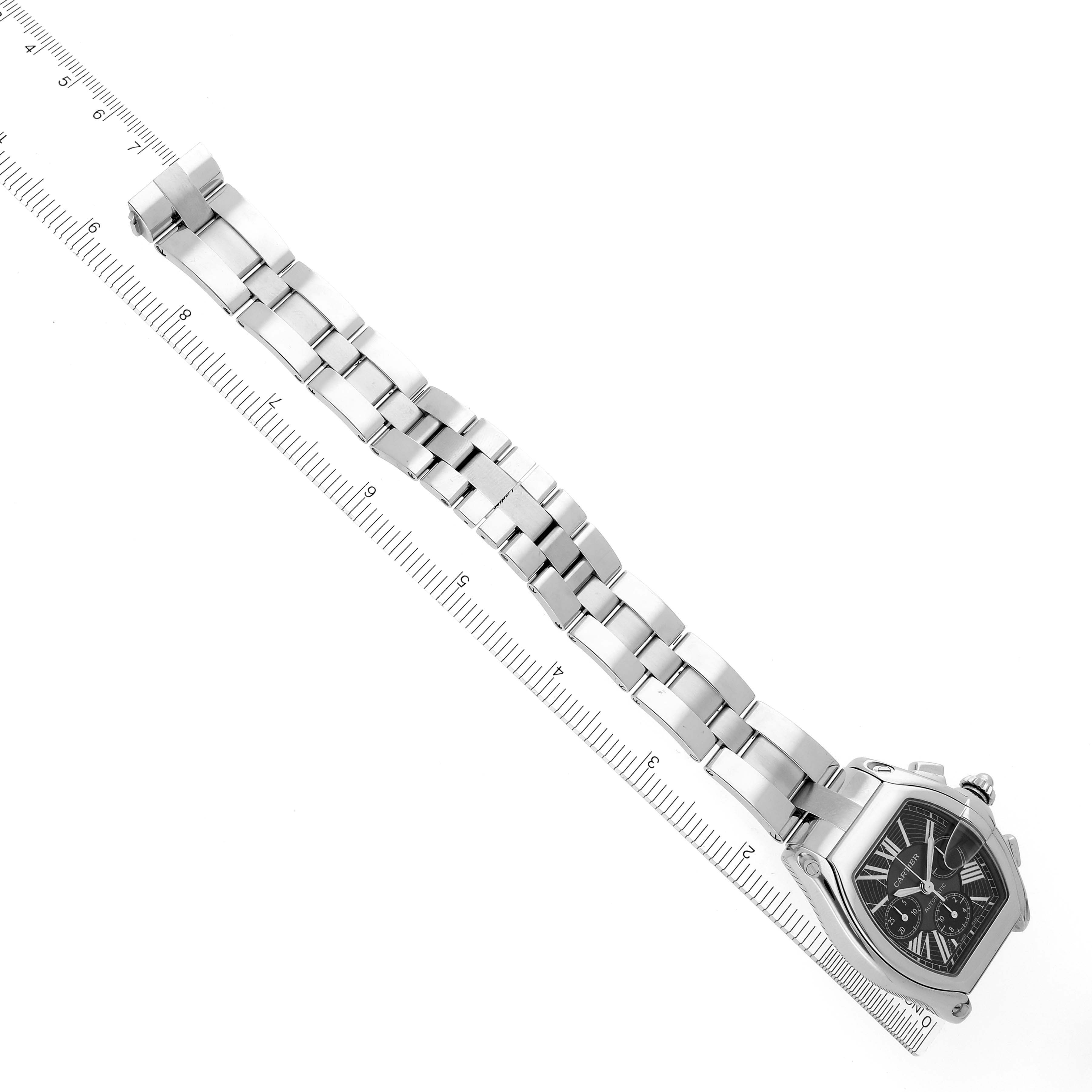 The image shows the Cartier Roadster W62020X6 Men's Stainless Steel Black Dial W62020X6 Men's Stainless Steel Black Dial watch at an angled top-down view, highlighting its bracelet and case next to a ruler.