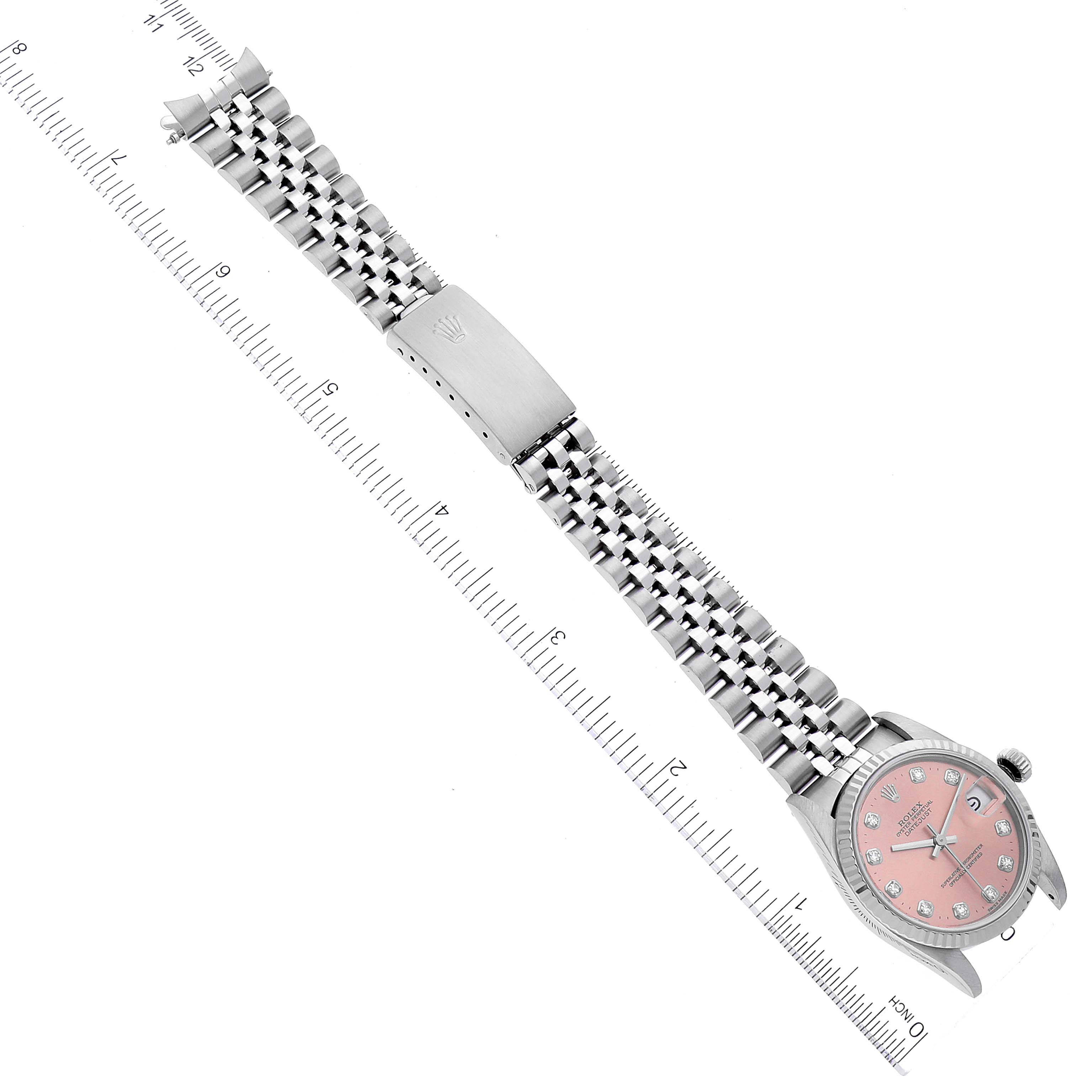 The image shows a Rolex Mid-Size 68274 Women
s Stainless Steel Pink Dial 68274 Women
s Stainless Steel Pink Dial watch laid flat with a pink dial, jubilee bracelet, and clasp, positioned diagonally against a ruler.