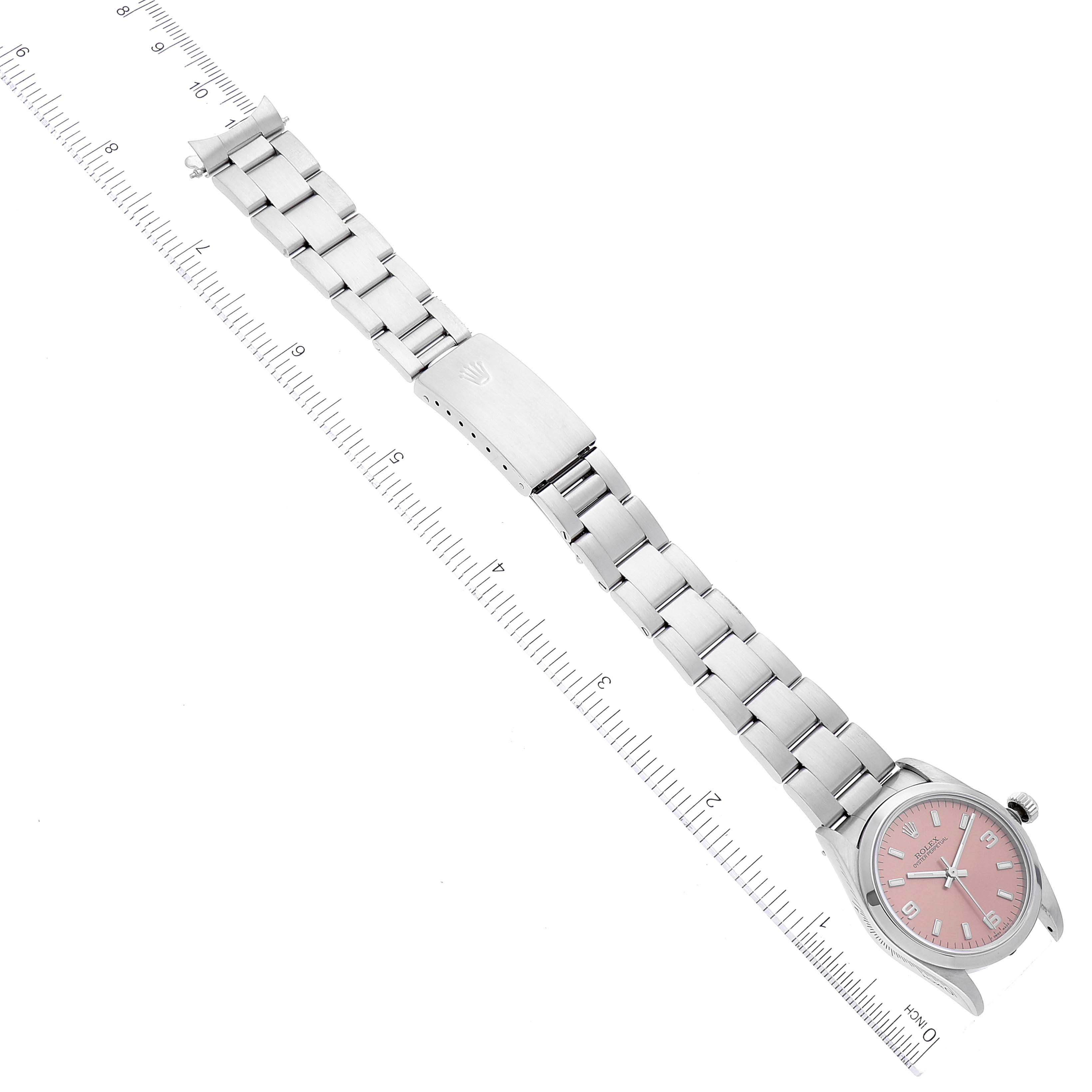 The image shows a Rolex Mid-Size 67480 Women
s Stainless Steel Pink Dial 67480 Women
s Stainless Steel Pink Dial model watch laid flat, displaying the watch face, bracelet, and clasp next to a measuring scale.