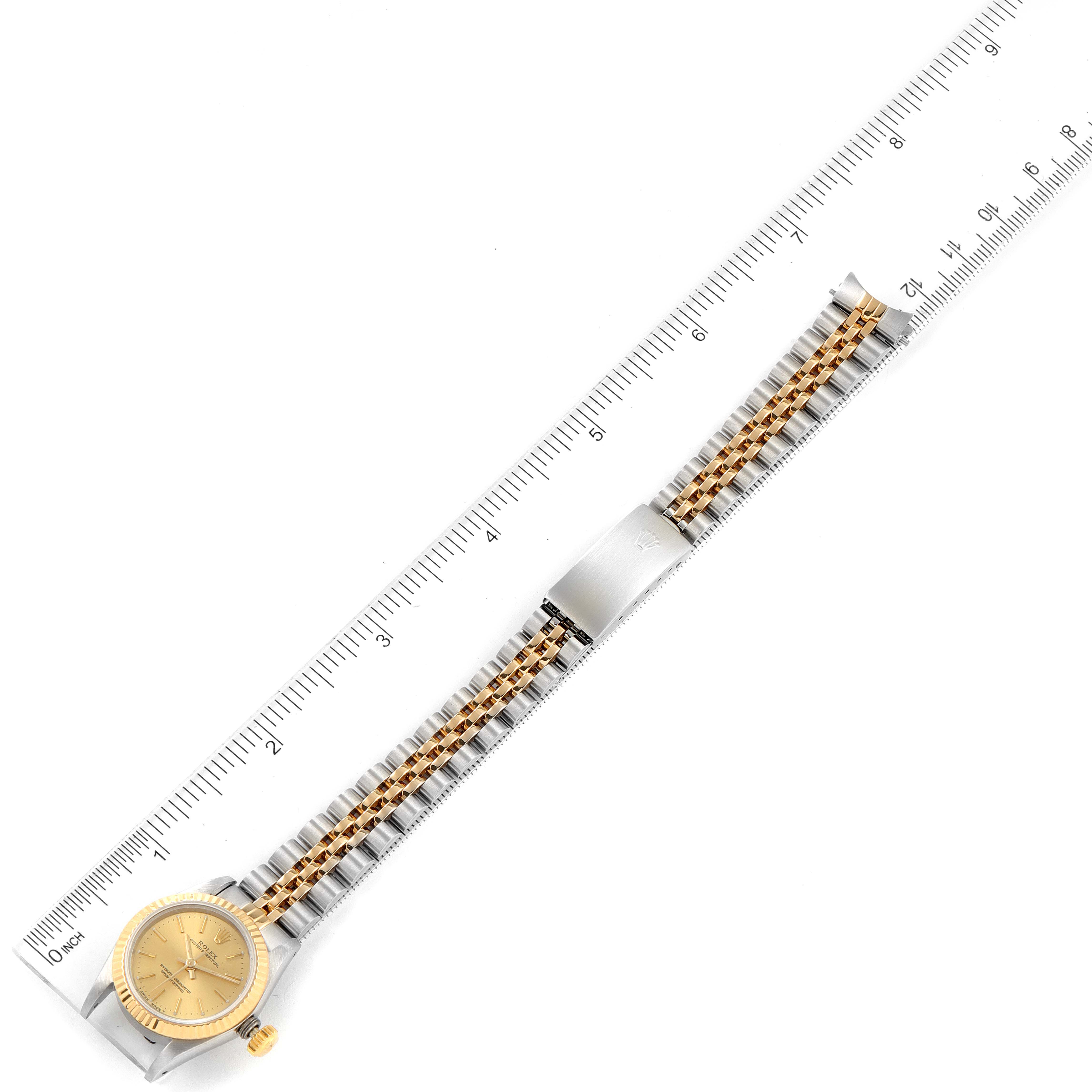 The image shows a top-down view of a Rolex Oyster Perpetual 67193 Women
s Steel and Gold (two tone) Champagne Dial 67193 Women
s Steel and Gold (two tone) Champagne Dial watch, including the face, band, and clasp, placed alongside a ruler.