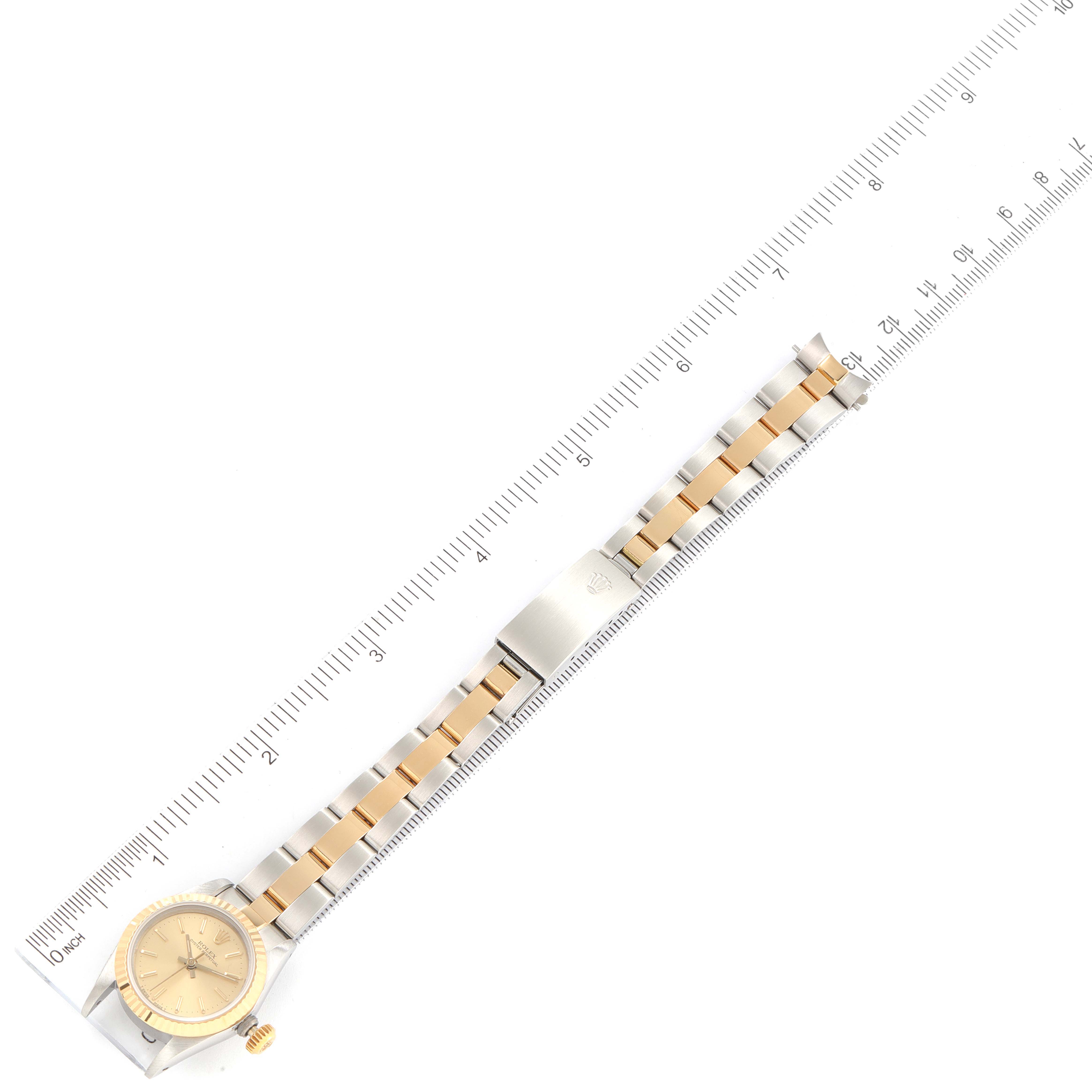 The Rolex Oyster Perpetual 67193 Women's Steel and Gold (two tone) Champagne Dial 67193 Women's Steel and Gold (two tone) Champagne Dial watch is shown laid flat next to a ruler, highlighting the watch face, bracelet, and clasp.