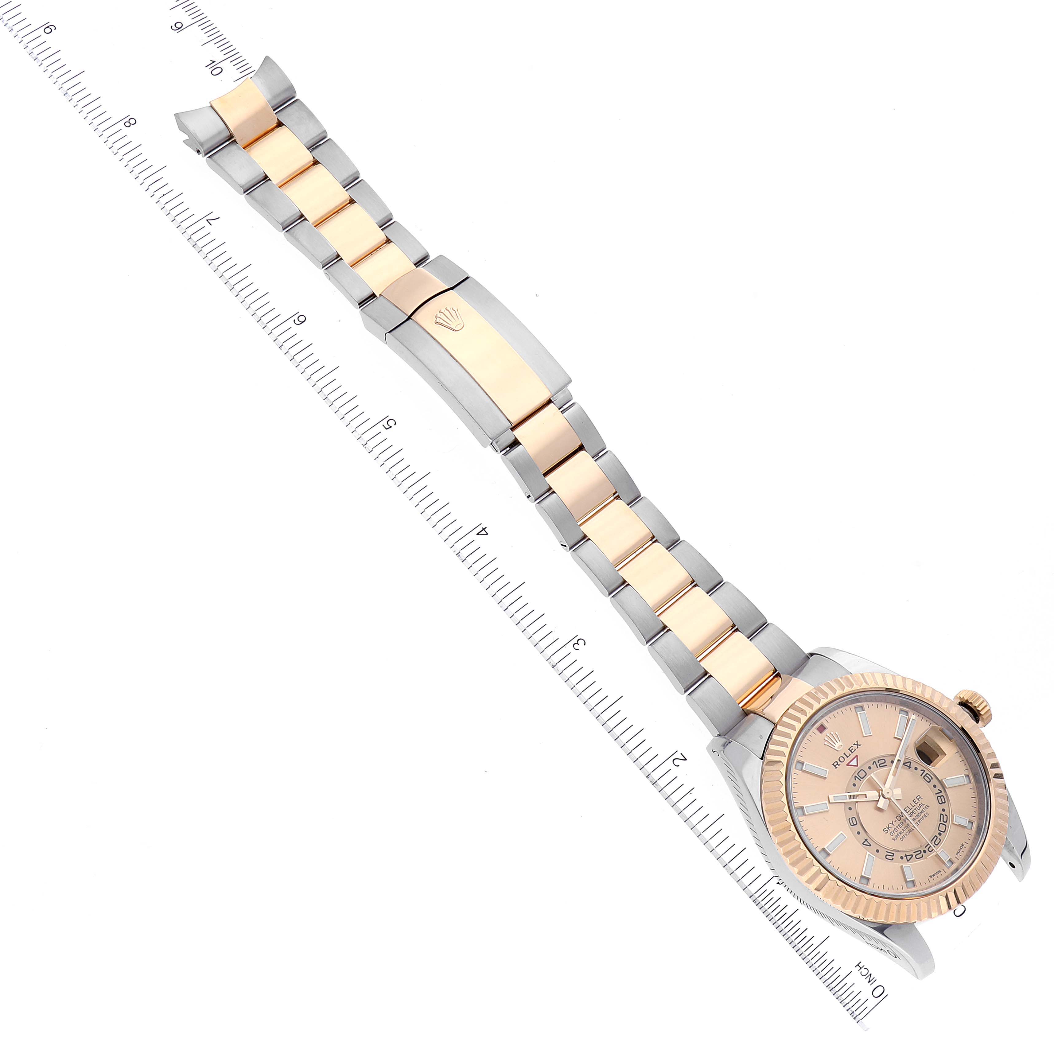 The image shows a Sky-Dweller model by Rolex, viewed from above, displaying the dial, bezel, and bracelet with a ruler for scale.