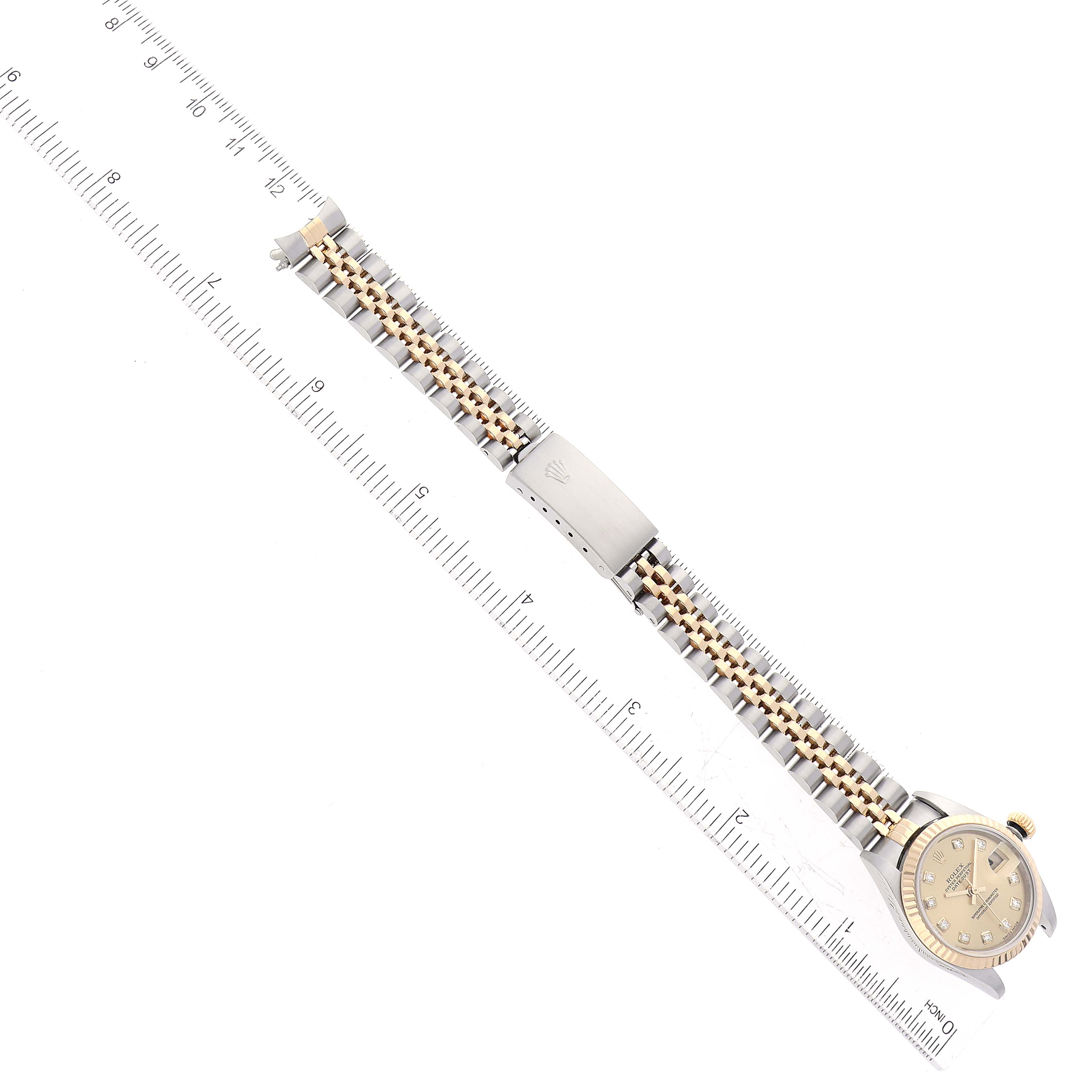 This image shows a Rolex Datejust 79173G Women's Steel and Gold (two tone) Champagne Dial 79173G Women's Steel and Gold (two tone) Champagne Dial watch laying flat with a clear view of its band and clasp, alongside a measuring ruler.