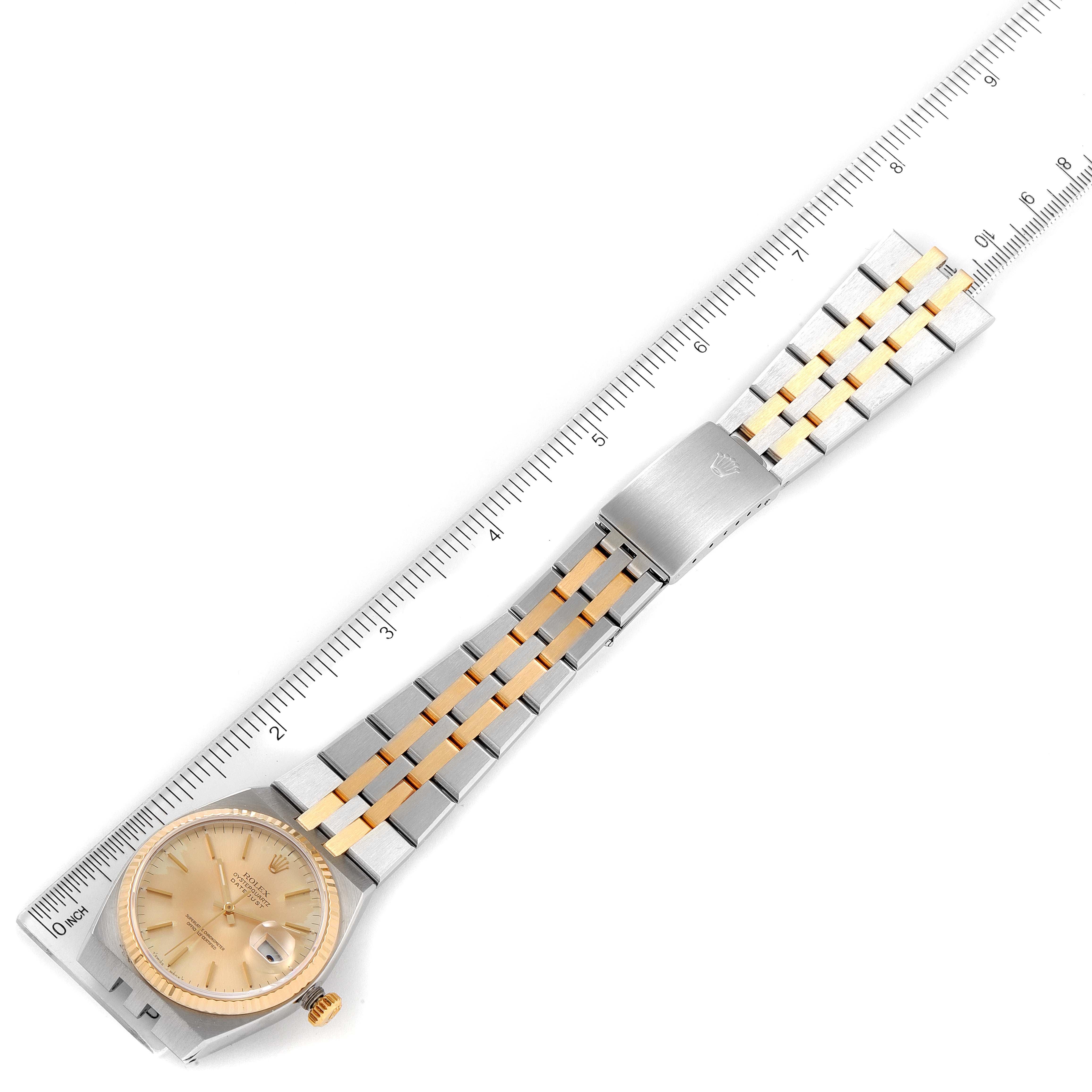 This image shows a Rolex Oysterquartz 17013 Men's Steel and Gold (two tone) Champagne Dial 17013 Men's Steel and Gold (two tone) Champagne Dial watch laid flat, displaying its bracelet, clasp, and dial, alongside a plastic ruler for measurement.