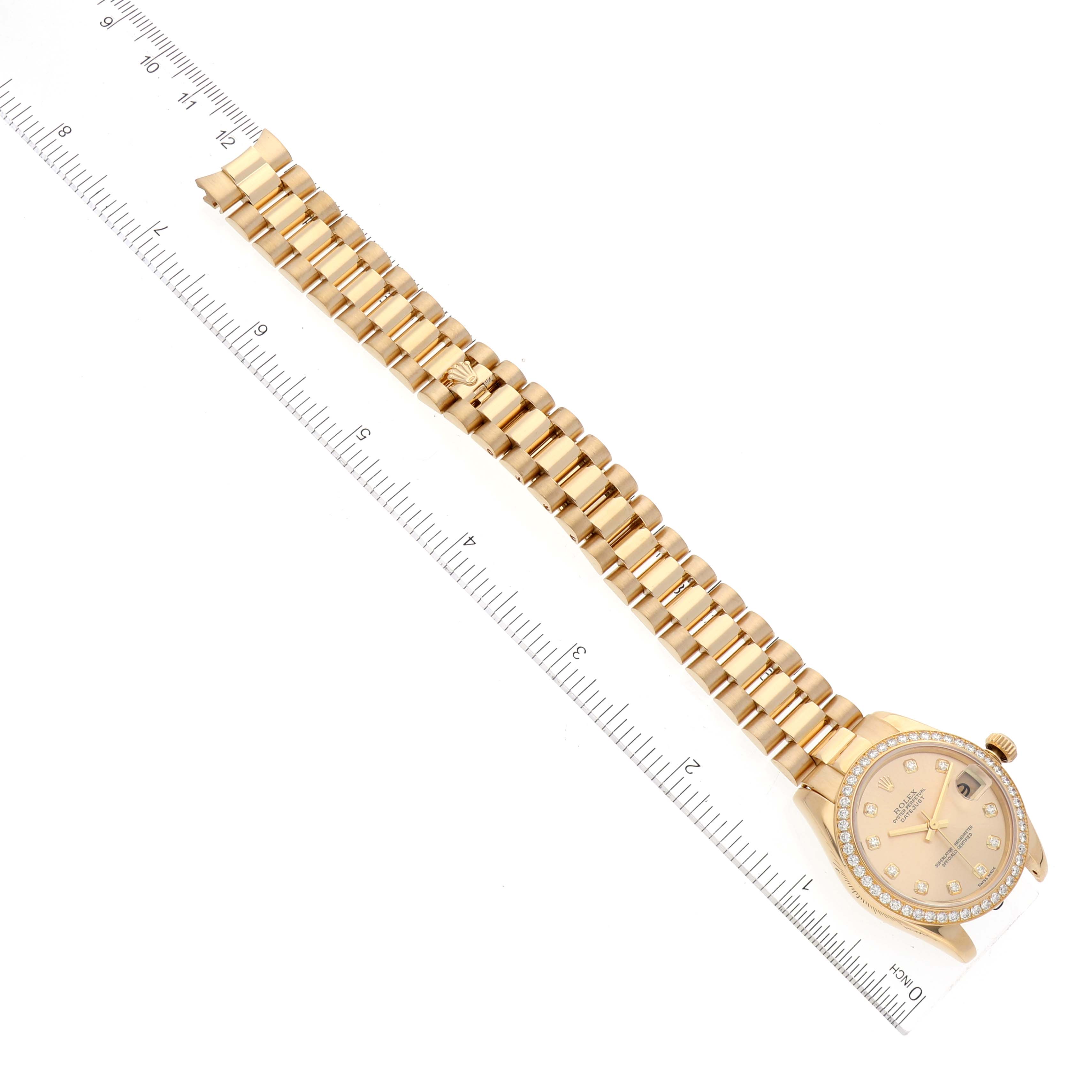 The photo shows a flat-lay view of a Rolex President 178288 Women
s Yellow Gold Champagne Dial 178288 Women
s Yellow Gold Champagne Dial model watch with its gold bracelet and dial against a measuring scale.