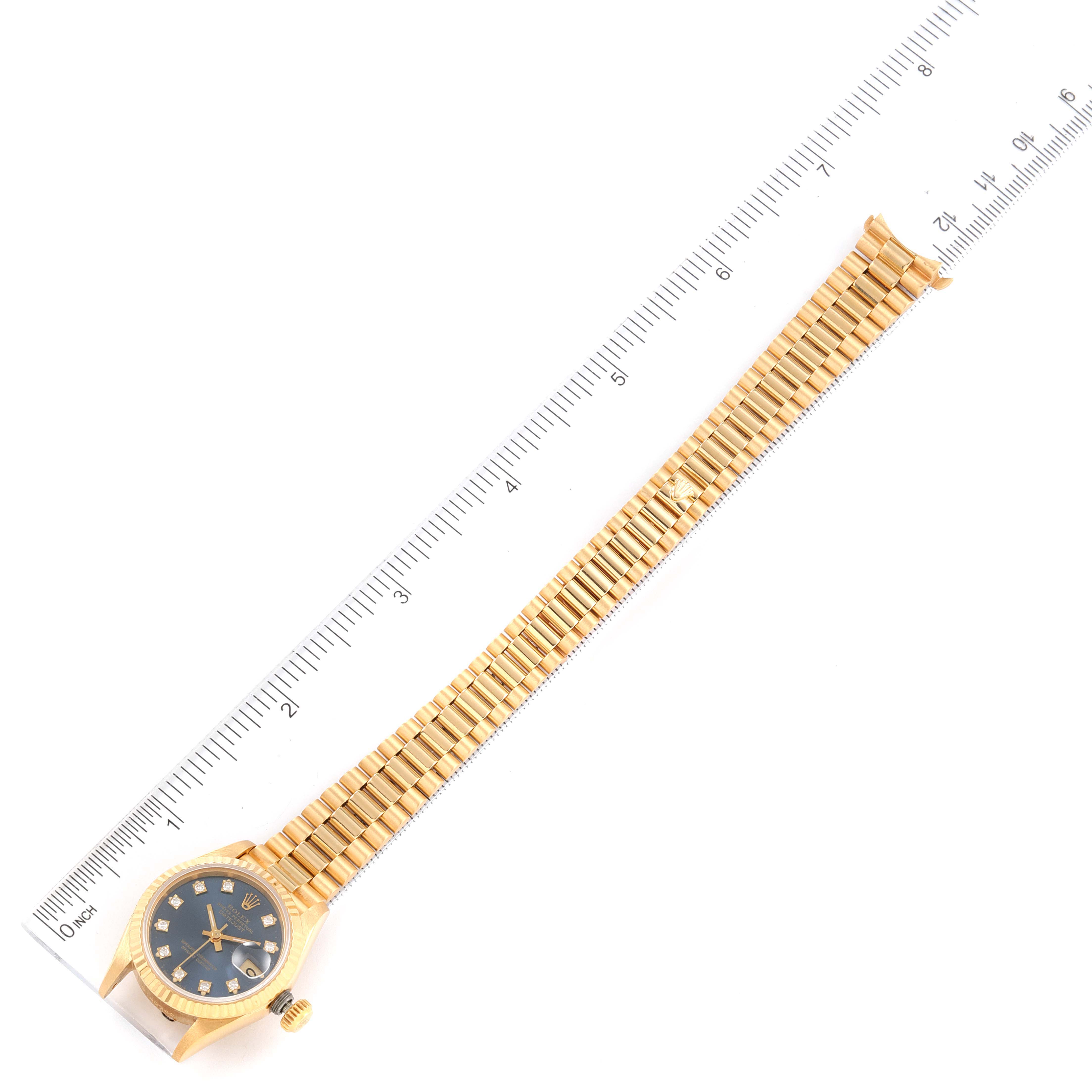 The image shows a full frontal angle of a Rolex President 69178 Women
s Yellow Gold Blue Dial 69178 Women
s Yellow Gold Blue Dial model watch, emphasizing its face, band, and crown, alongside a measuring ruler.