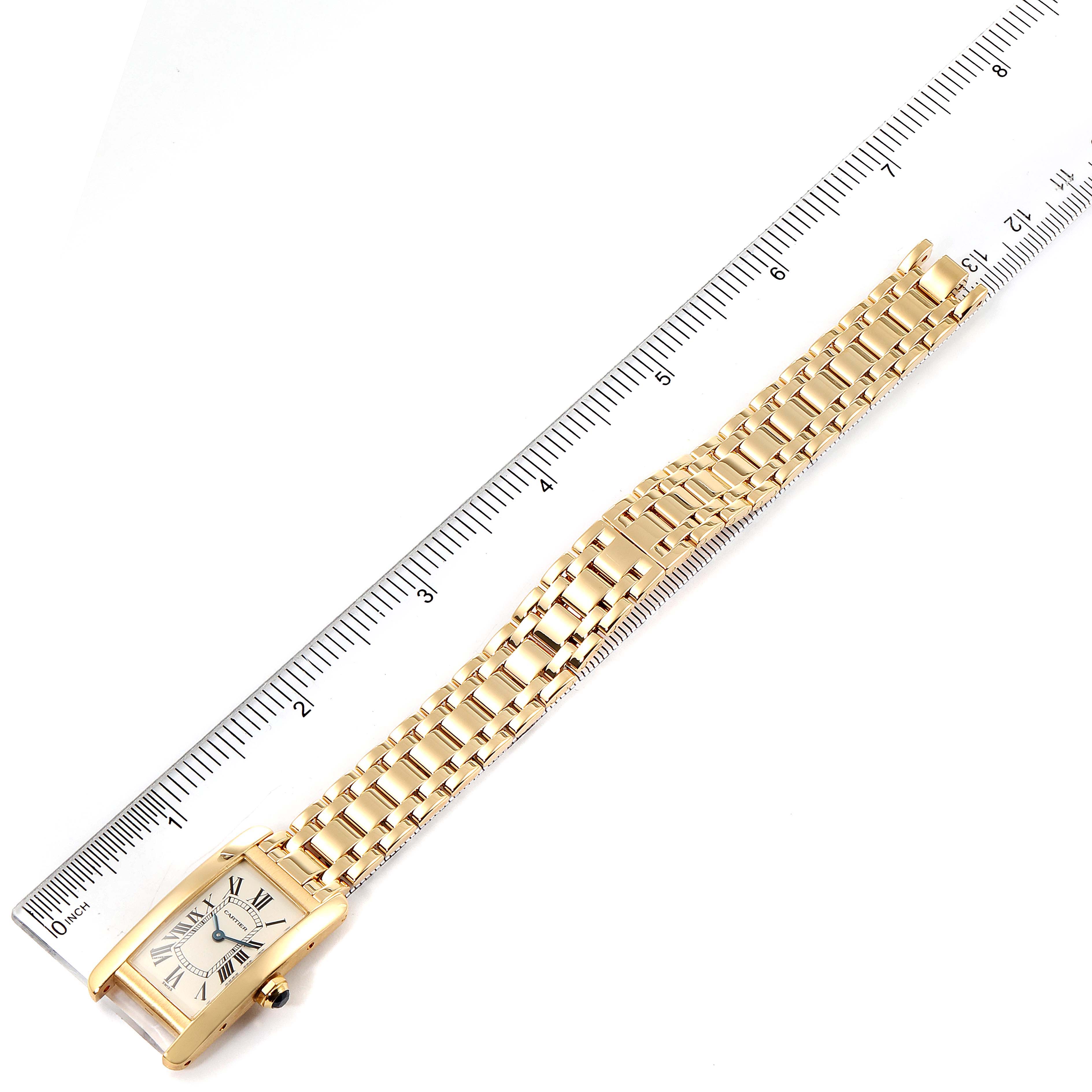 The Cartier Tank Americaine W26015K2 Women's Yellow Gold Silver Dial W26015K2 Women's Yellow Gold Silver Dial watch is shown from a top-down angle, displaying the face and full gold bracelet on a ruler.