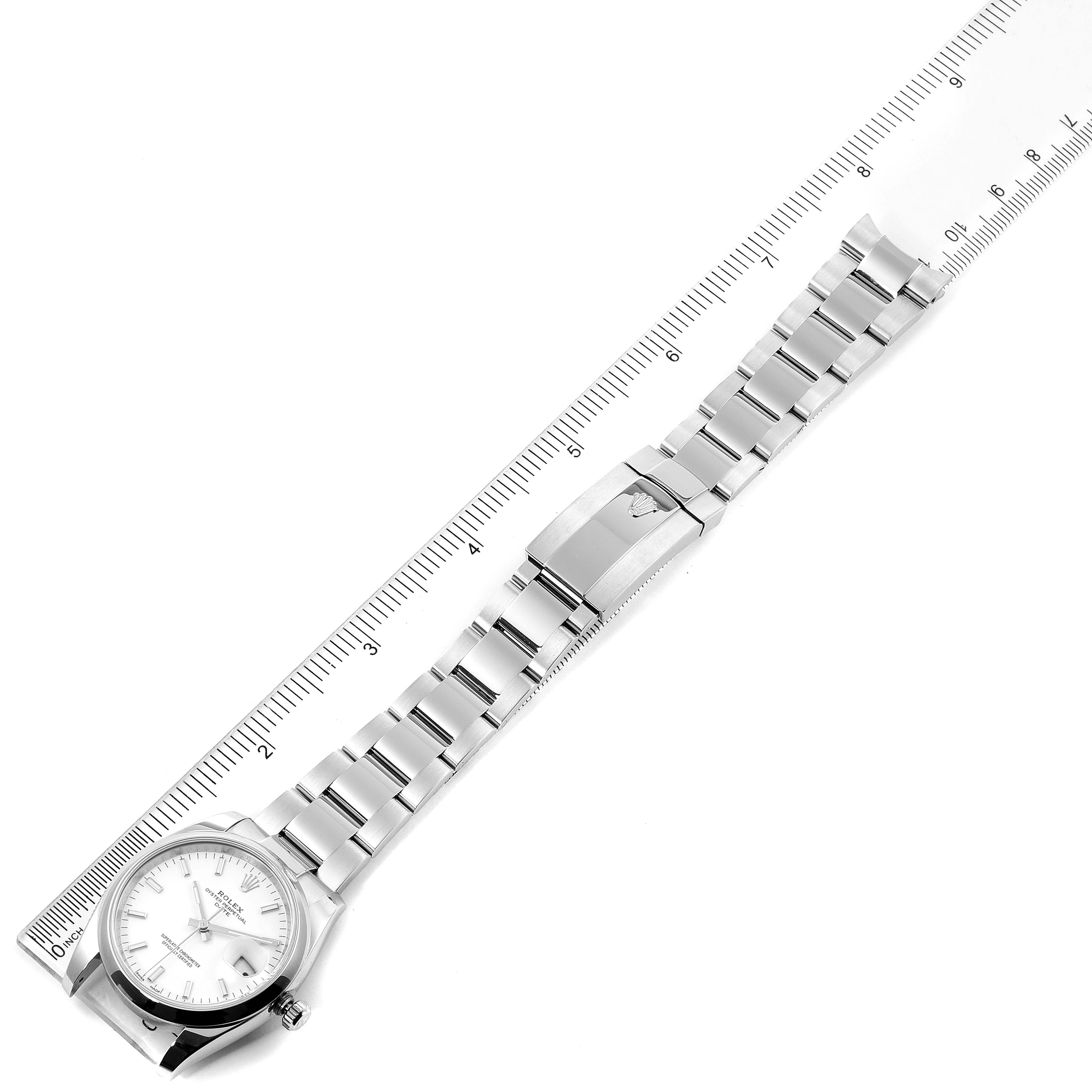 The image shows a Rolex Date 115200 Men's Stainless Steel White Dial 115200 Men's Stainless Steel White Dial model watch laid flat with its face, bracelet, and clasp visible, next to a ruler for scale.