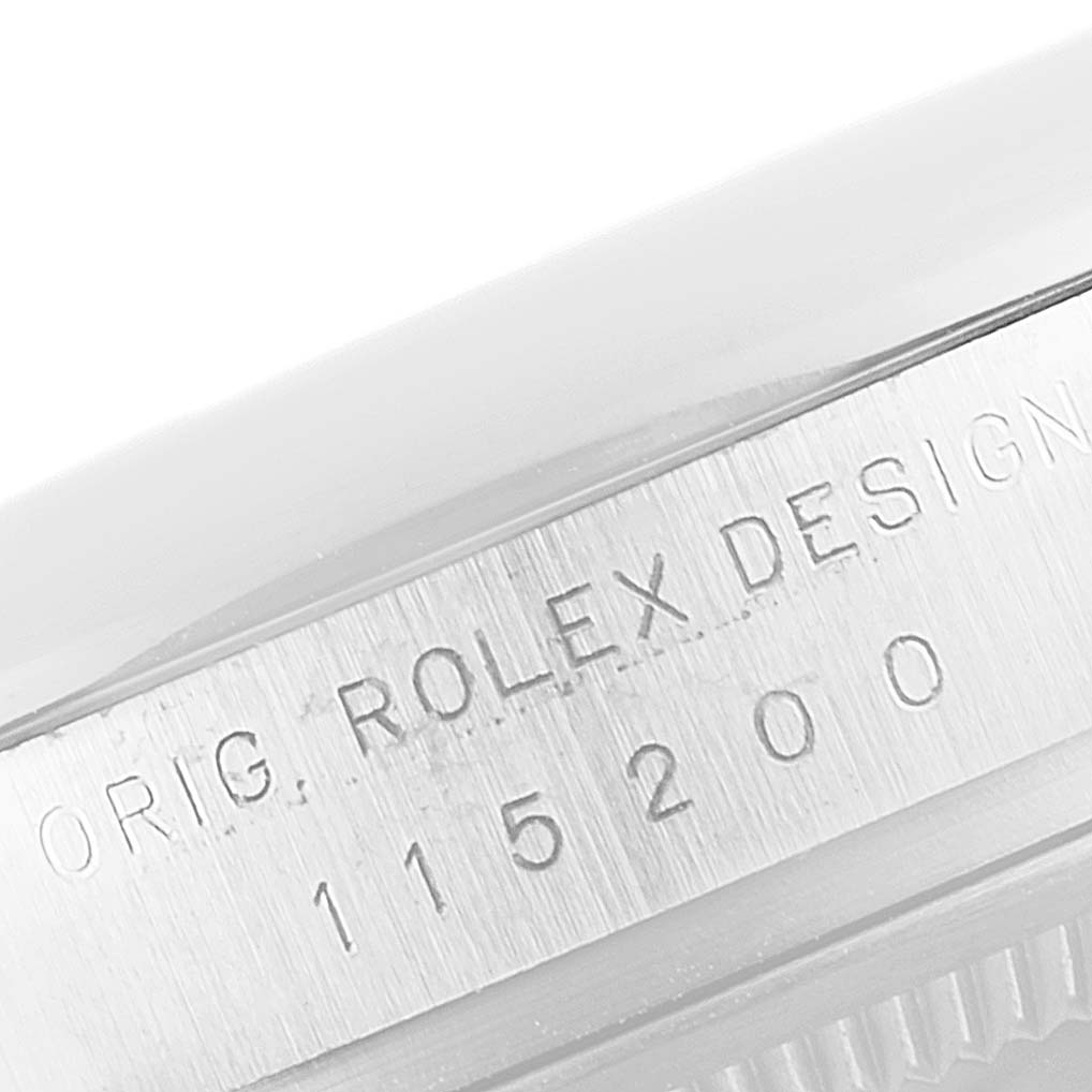 This close-up shows the engraved serial number on the case side of a Rolex Date 115200 Men's Stainless Steel White Dial 115200 Men's Stainless Steel White Dial watch.