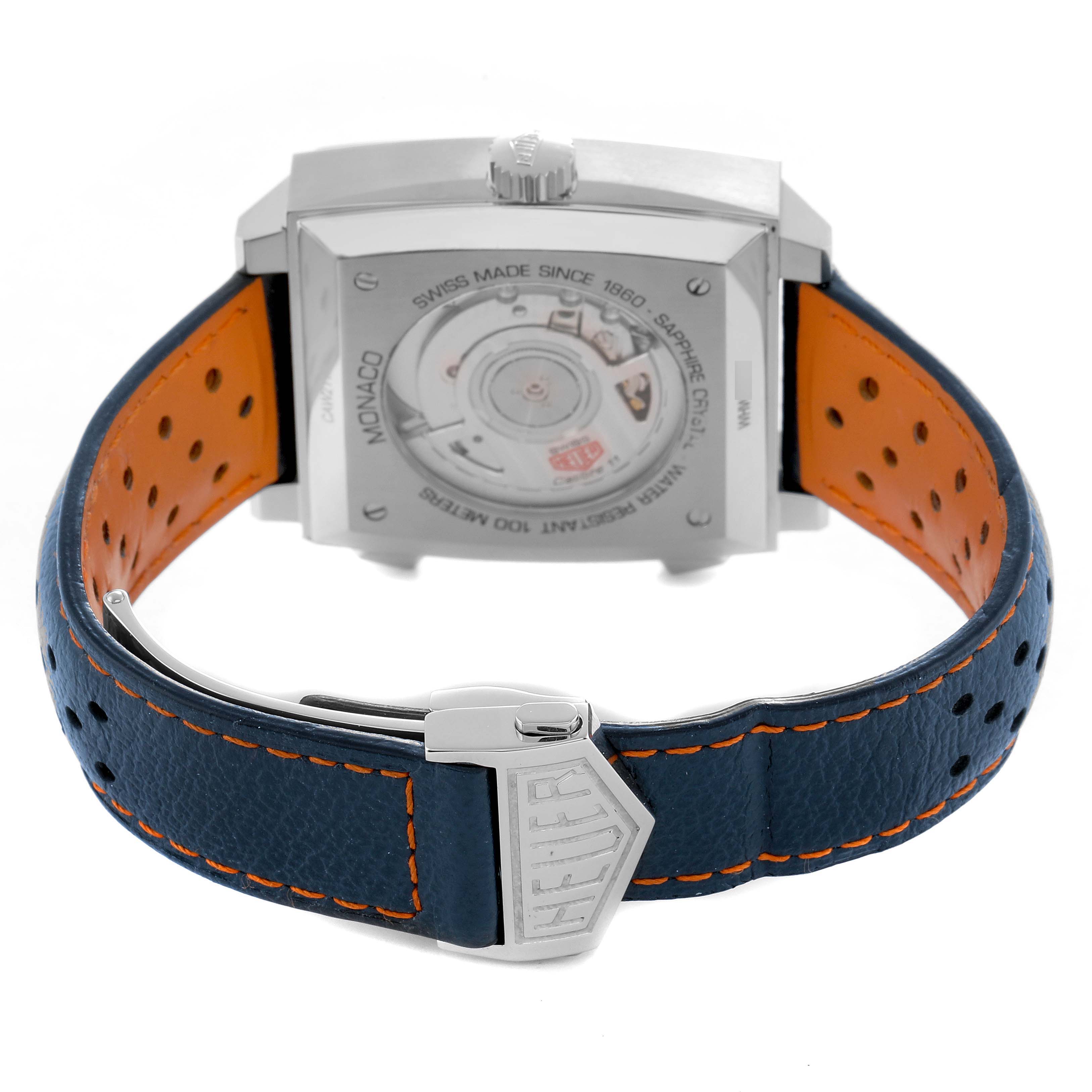 The image shows the back case, movement, and perforated strap of a Tag Heuer Monaco CAW211R Men's Stainless Steel Blue Dial watch at a slight rear angle.