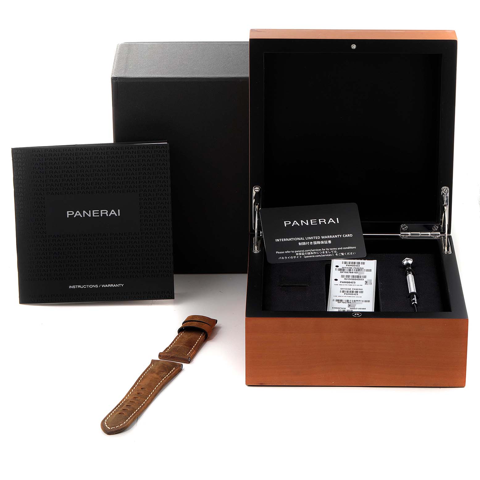 The image shows a Panerai Luminor PAM00423 Men
s Stainless Steel Black Dial PAM00423 Men
s Stainless Steel Black Dial watch box with warranty cards, an extra strap, and a tool from a top-down angle.