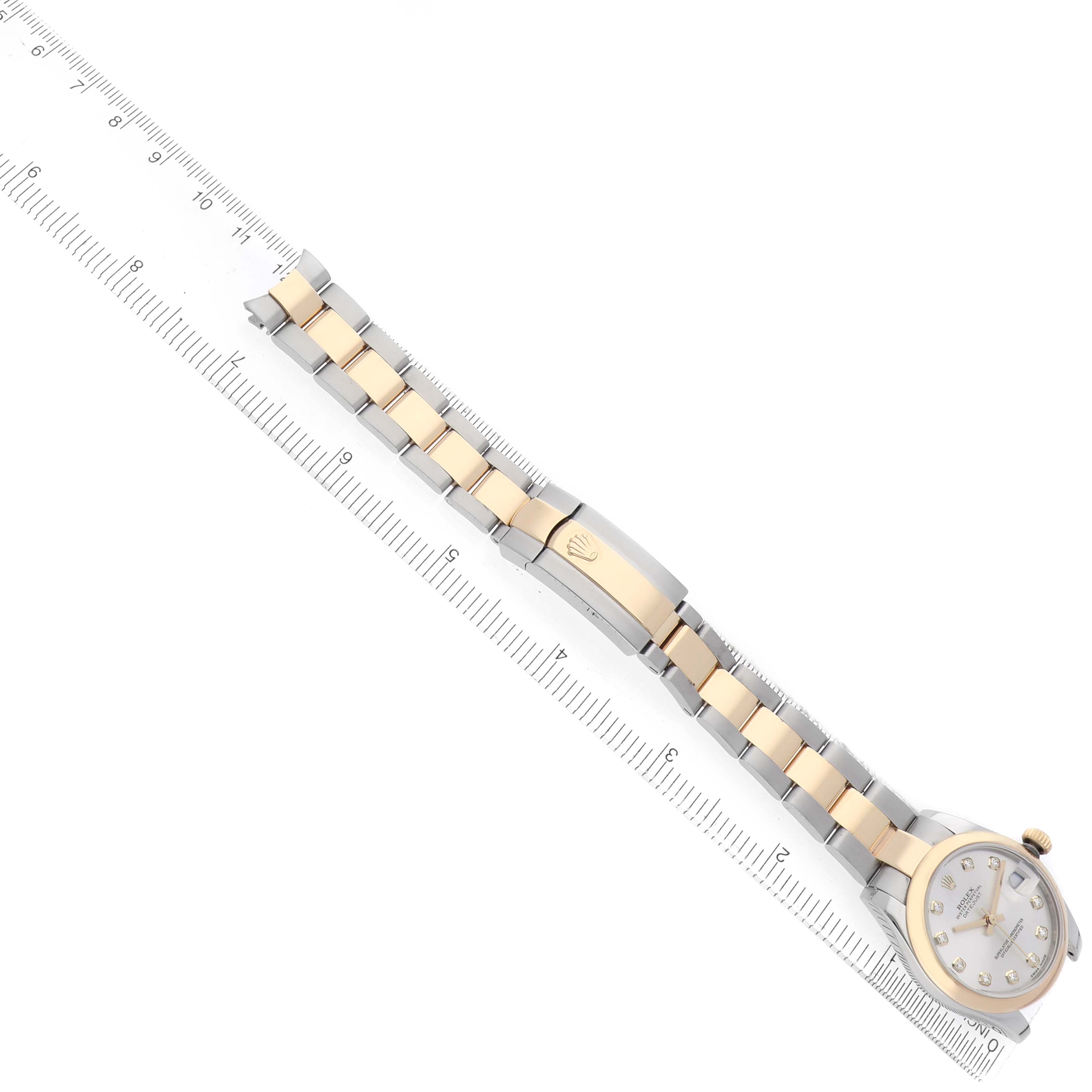 The Rolex Mid-Size 178243 Women's Steel and Gold (two tone) Silver Dial watch is shown diagonally, displaying the full bracelet and face, alongside a ruler for scale.