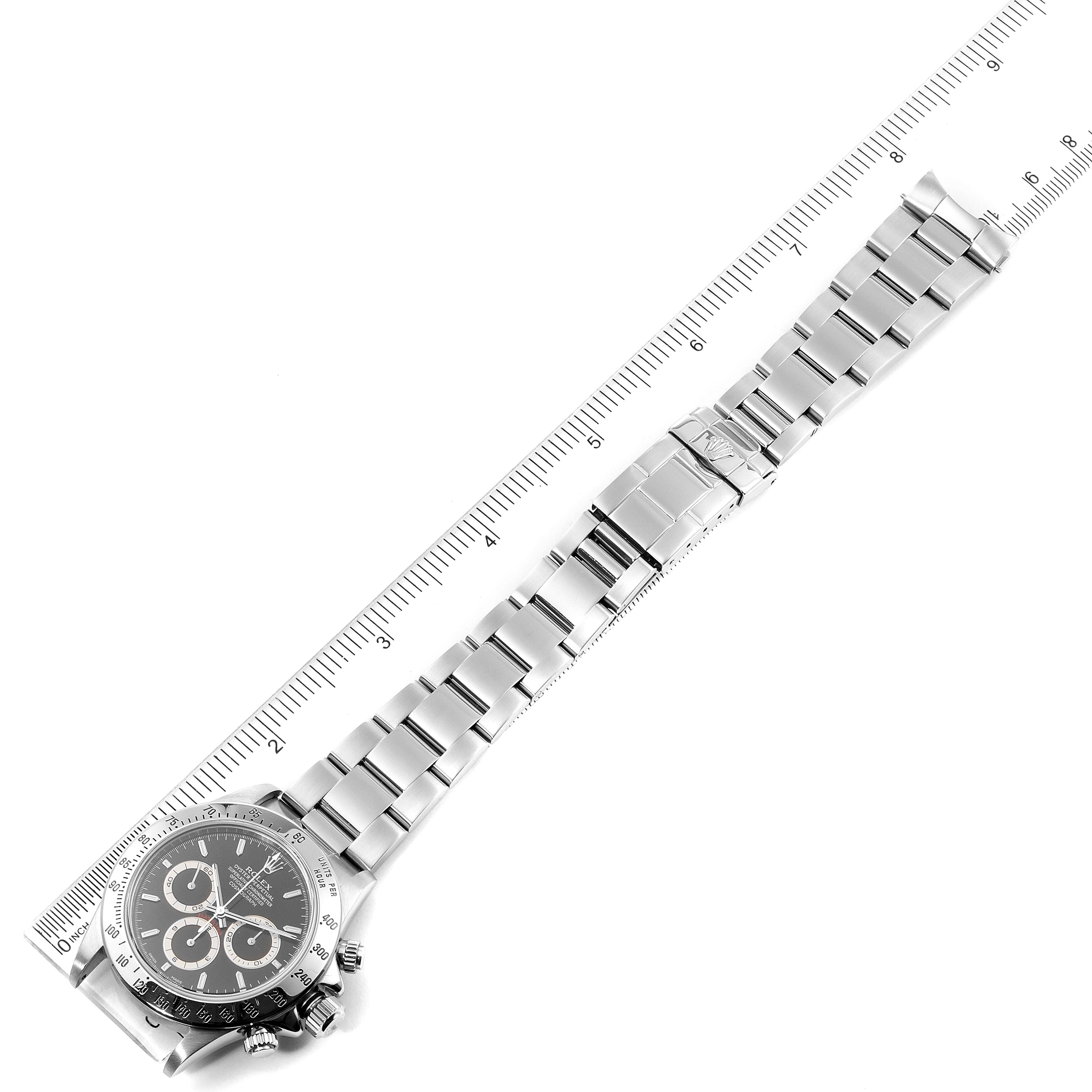 The Rolex Daytona 16520 Men's Stainless Steel Black Dial 16520 Men's Stainless Steel Black Dial watch is shown in a top-down angle with its full bracelet and clasp visible, alongside a ruler.