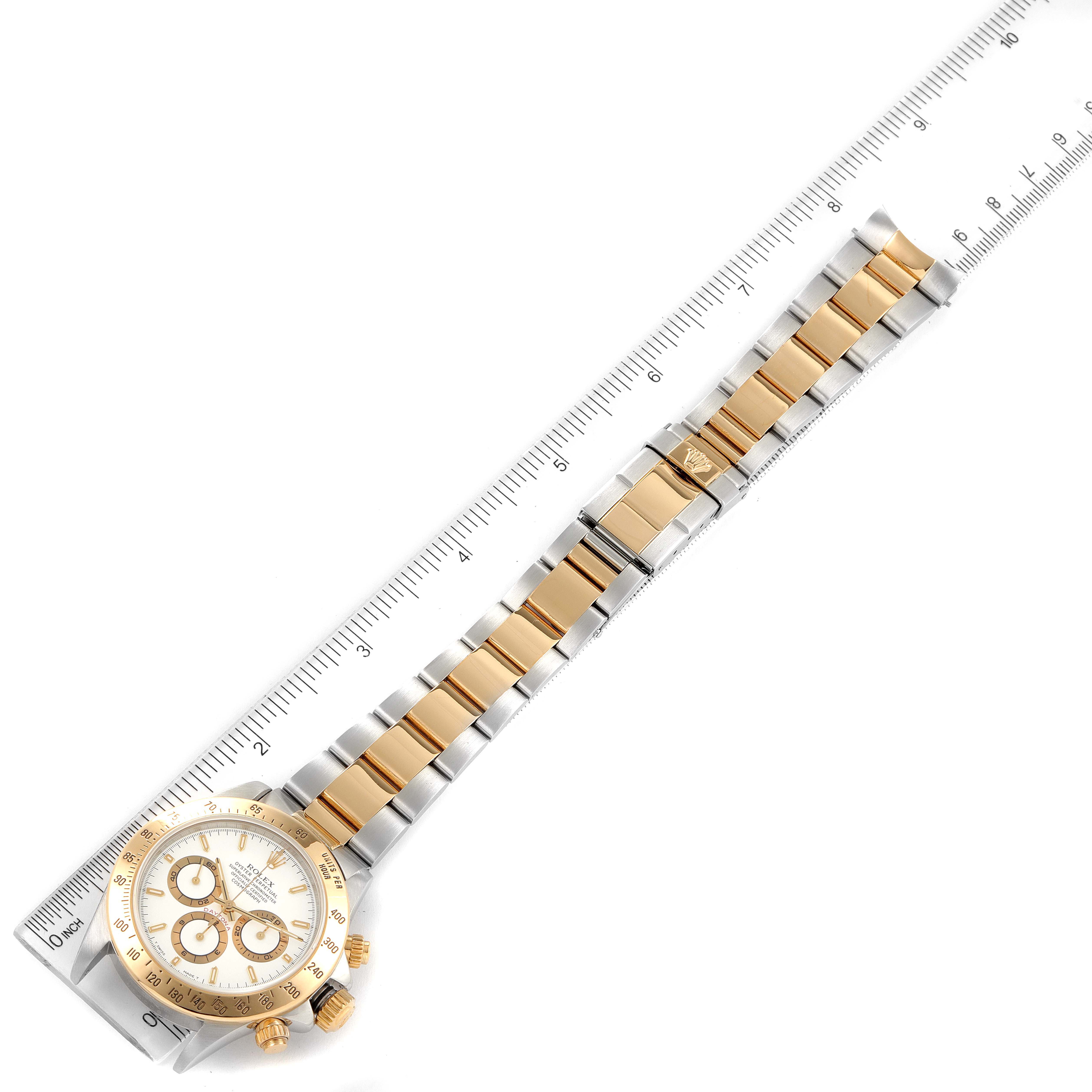 The image shows an overhead view of a Rolex Daytona 16523 Men
s Steel and Gold (two tone) White Dial 16523 Men
s Steel and Gold (two tone) White Dial watch, including its full band and ruler for scale.