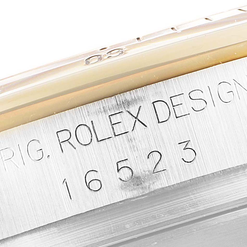 The image shows a close-up of the side of a Rolex Daytona 16523 Men
s Steel and Gold (two tone) White Dial 16523 Men
s Steel and Gold (two tone) White Dial watch, highlighting the model number and part of the bezel.