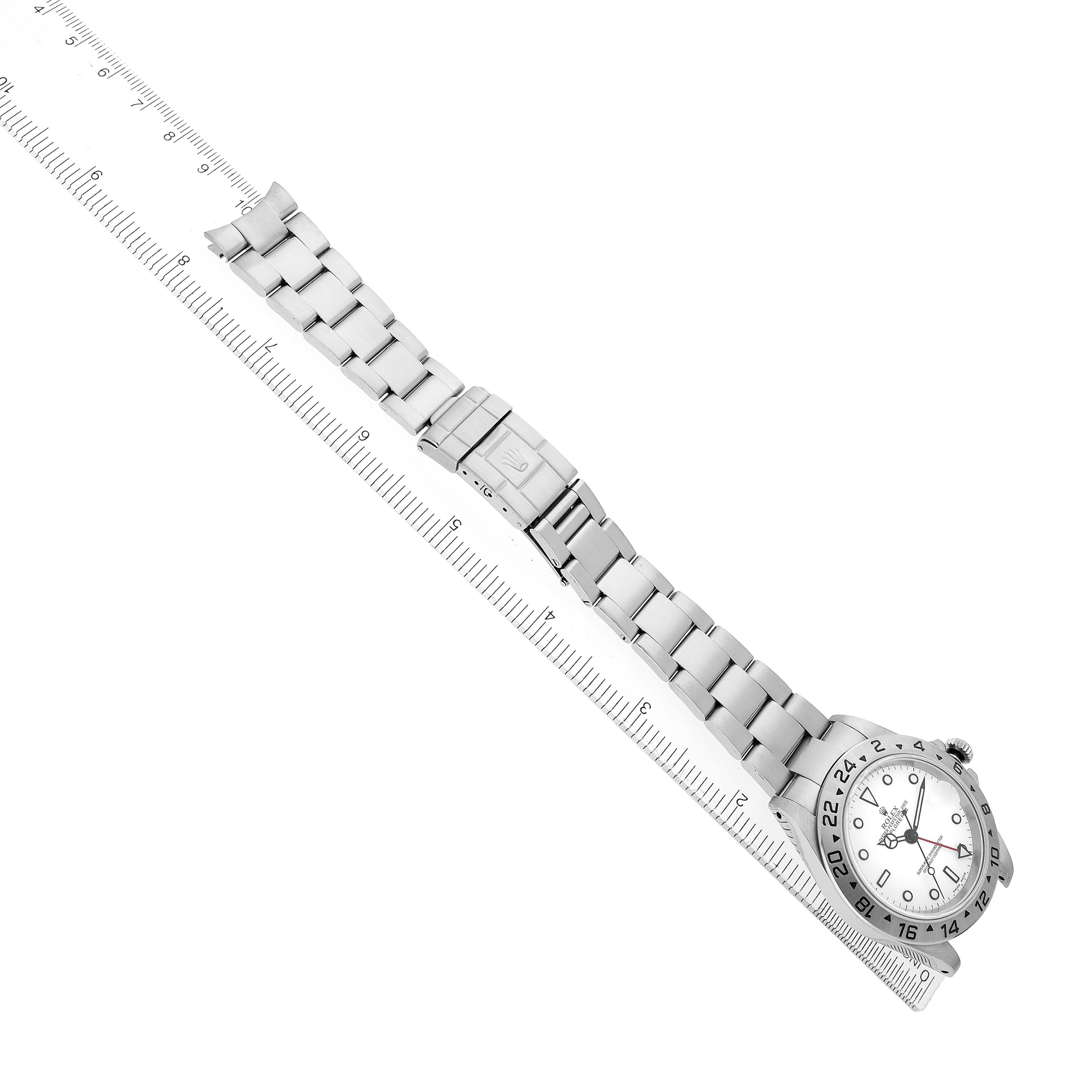 The Rolex Explorer 16570 Men's Stainless Steel White Dial watch is angled diagonally, showing its face, bezel, and full bracelet alongside a measuring ruler.