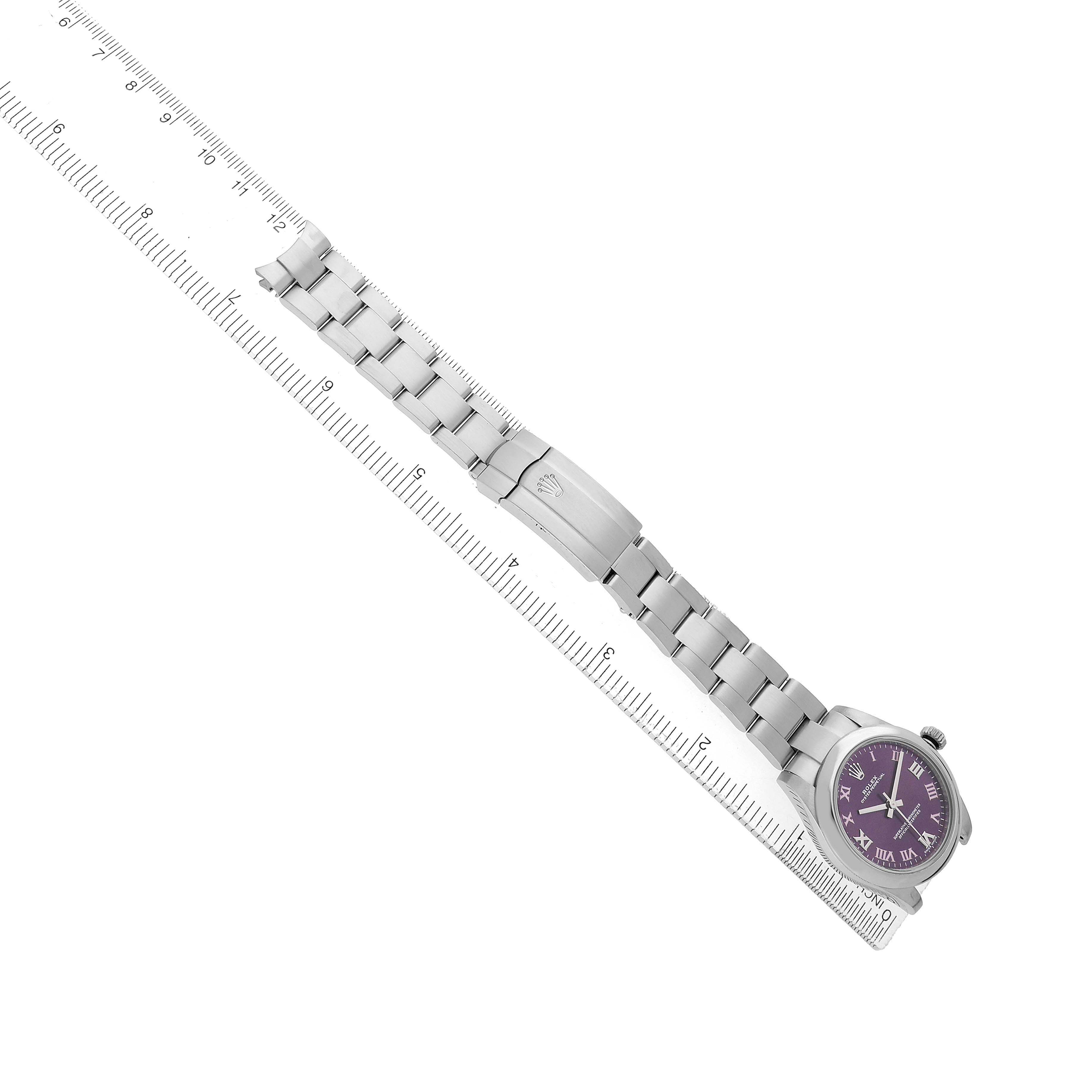 The Rolex Oyster Perpetual 177200 Women's Stainless Steel Purple Dial watch is shown at an angle, displaying its bracelet and purple dial beside a ruler for scale.