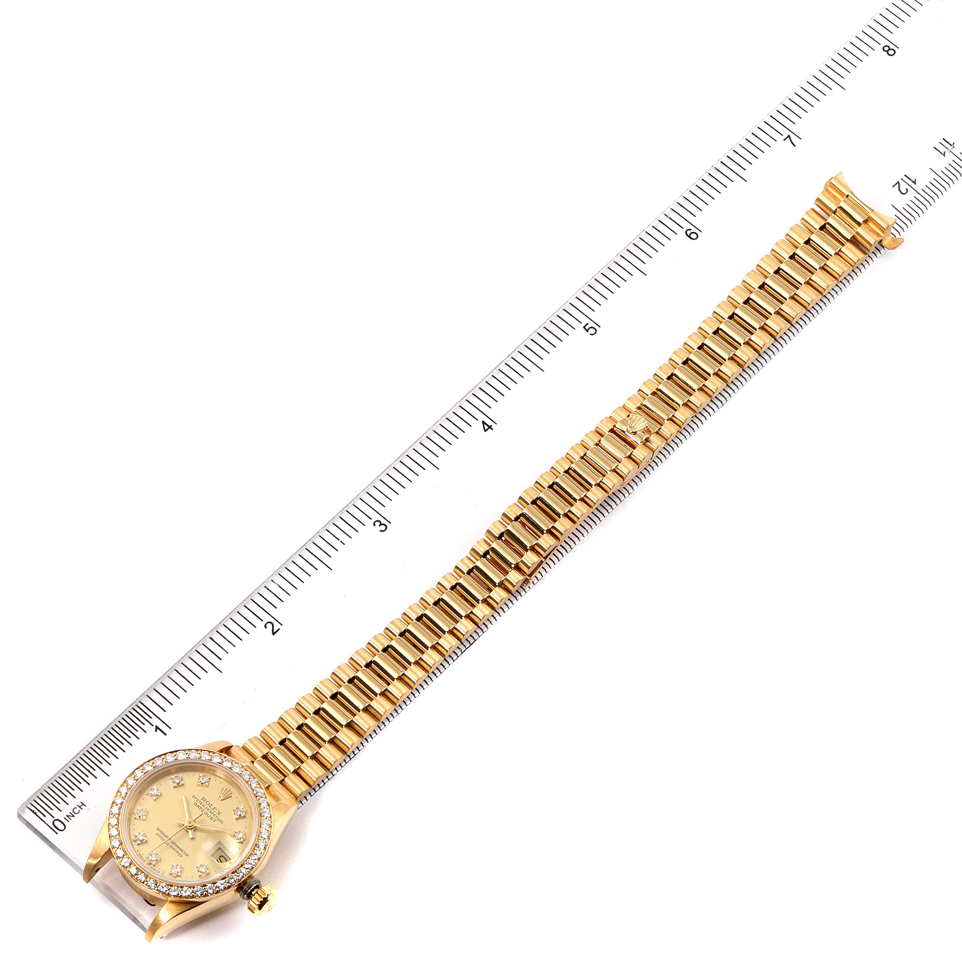 This image shows a Rolex President 69138 Women
s Yellow Gold Champagne Dial 69138 Women
s Yellow Gold Champagne Dial model watch laid flat next to a ruler, displaying its dial, bezel, and bracelet.