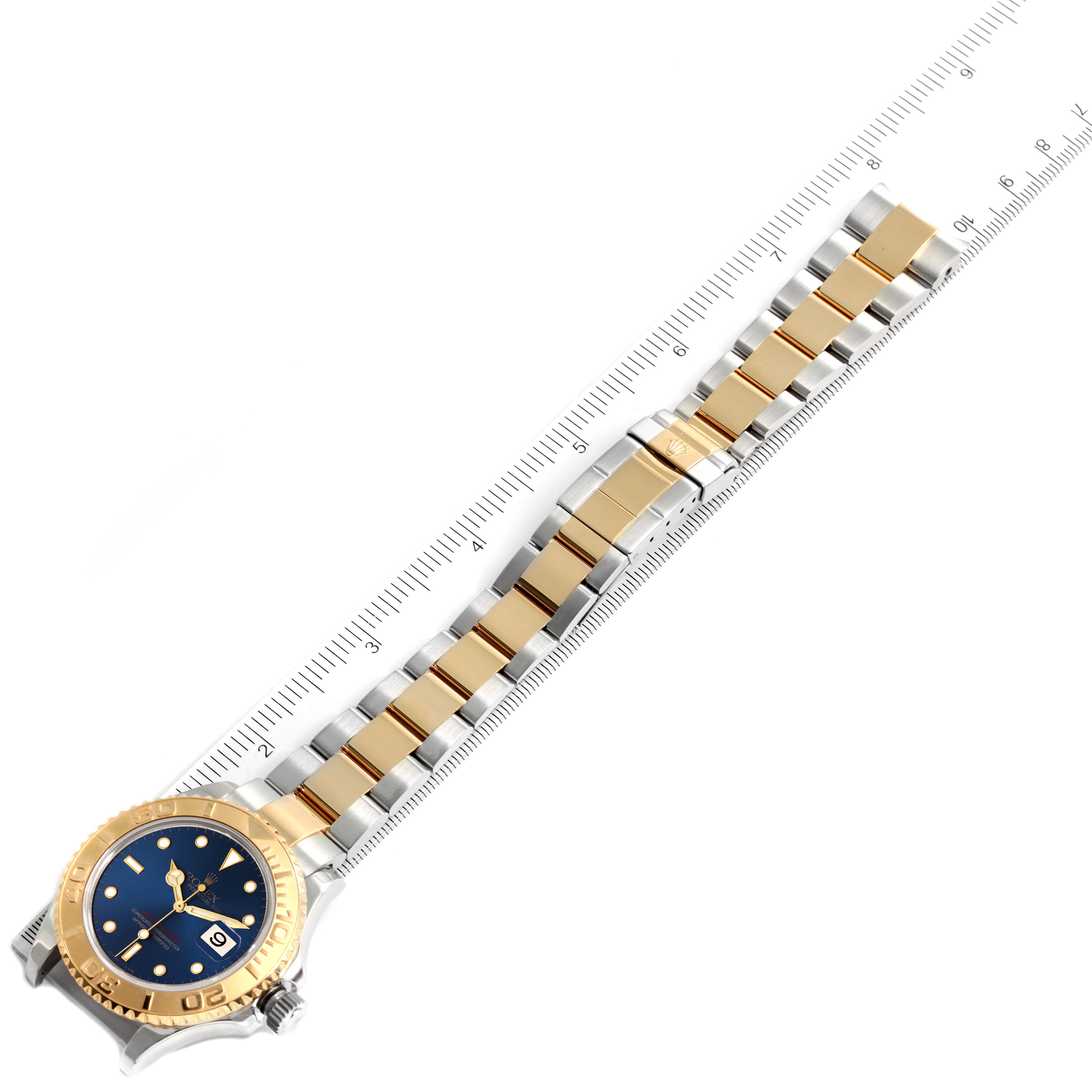 This image shows a Rolex Yacht-Master 16623 Men's Steel and Gold (two tone) Blue Dial 16623 Men's Steel and Gold (two tone) Blue Dial watch laid flat, showcasing the blue dial, gold bezel, and two-tone bracelet next to a ruler.