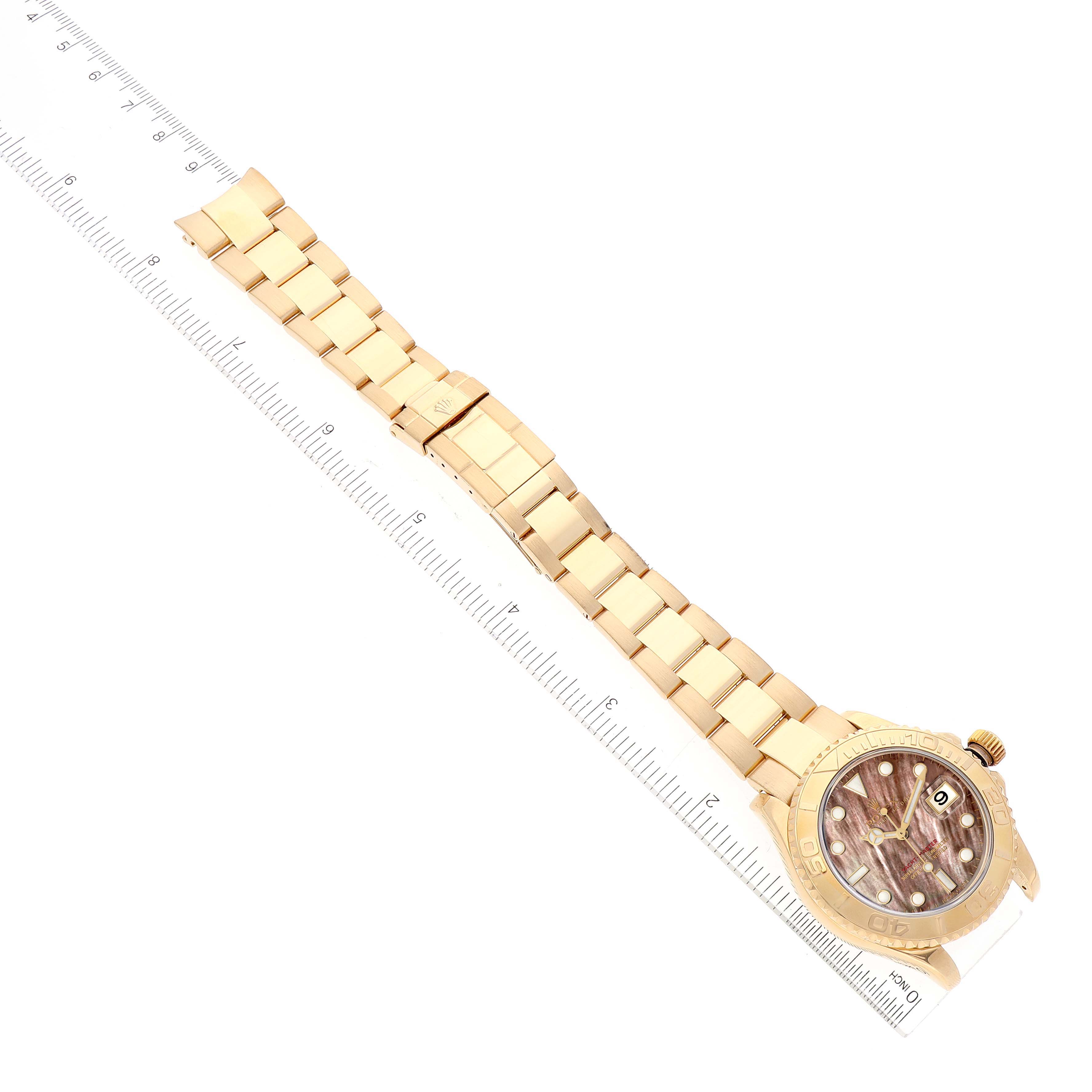 This image shows a Rolex Yacht-Master 16628 Men's Yellow Gold Mother of Pearl Dial 16628 Men's Yellow Gold Mother of Pearl Dial watch laid flat at an angle, displaying its band and face with a ruler underneath.