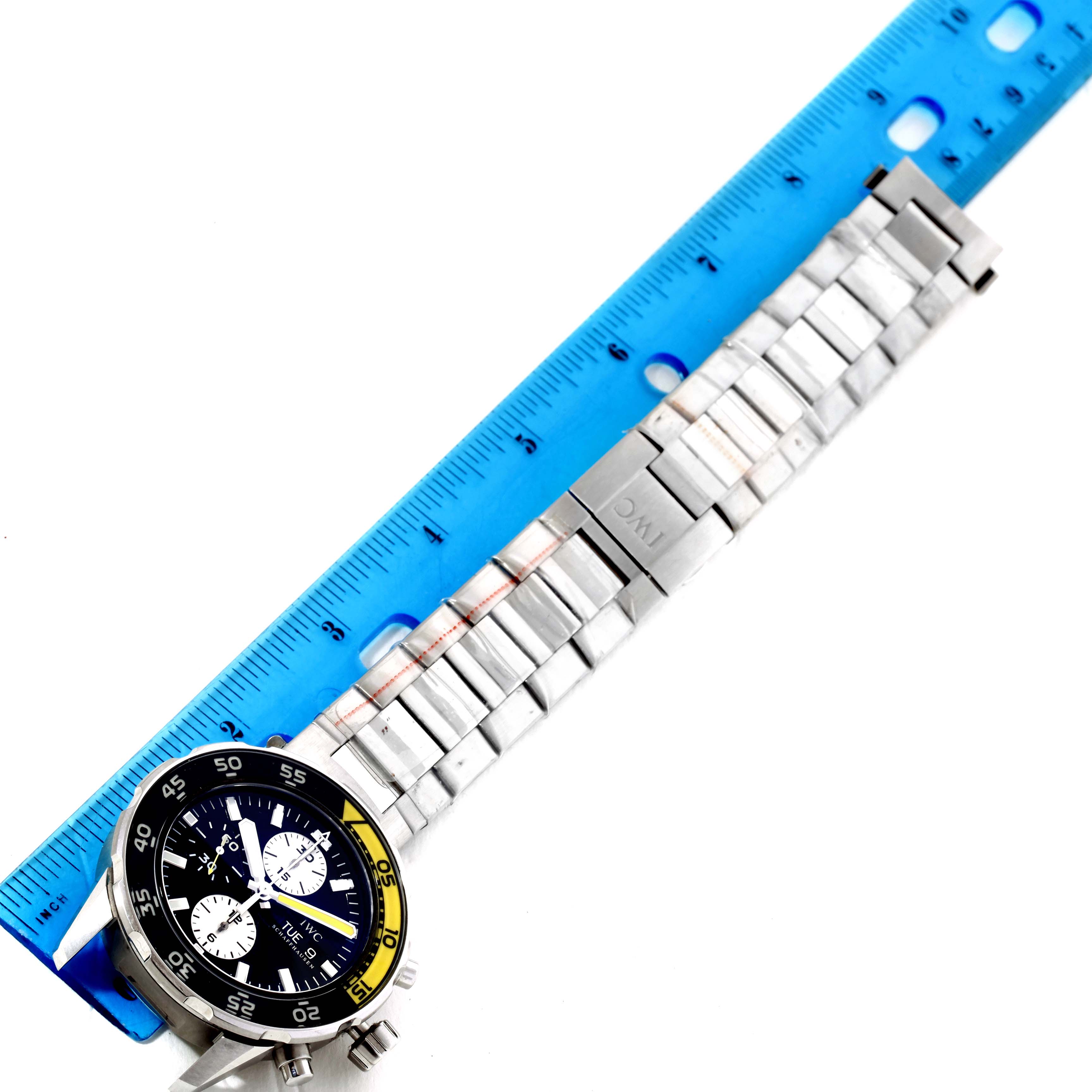 The image shows an IWC Aquatimer IW376701 Men's Stainless Steel Black Dial IW376701 Men's Stainless Steel Black Dial watch lying flat with a blue ruler, displaying the full length of its metal bracelet and watch face.