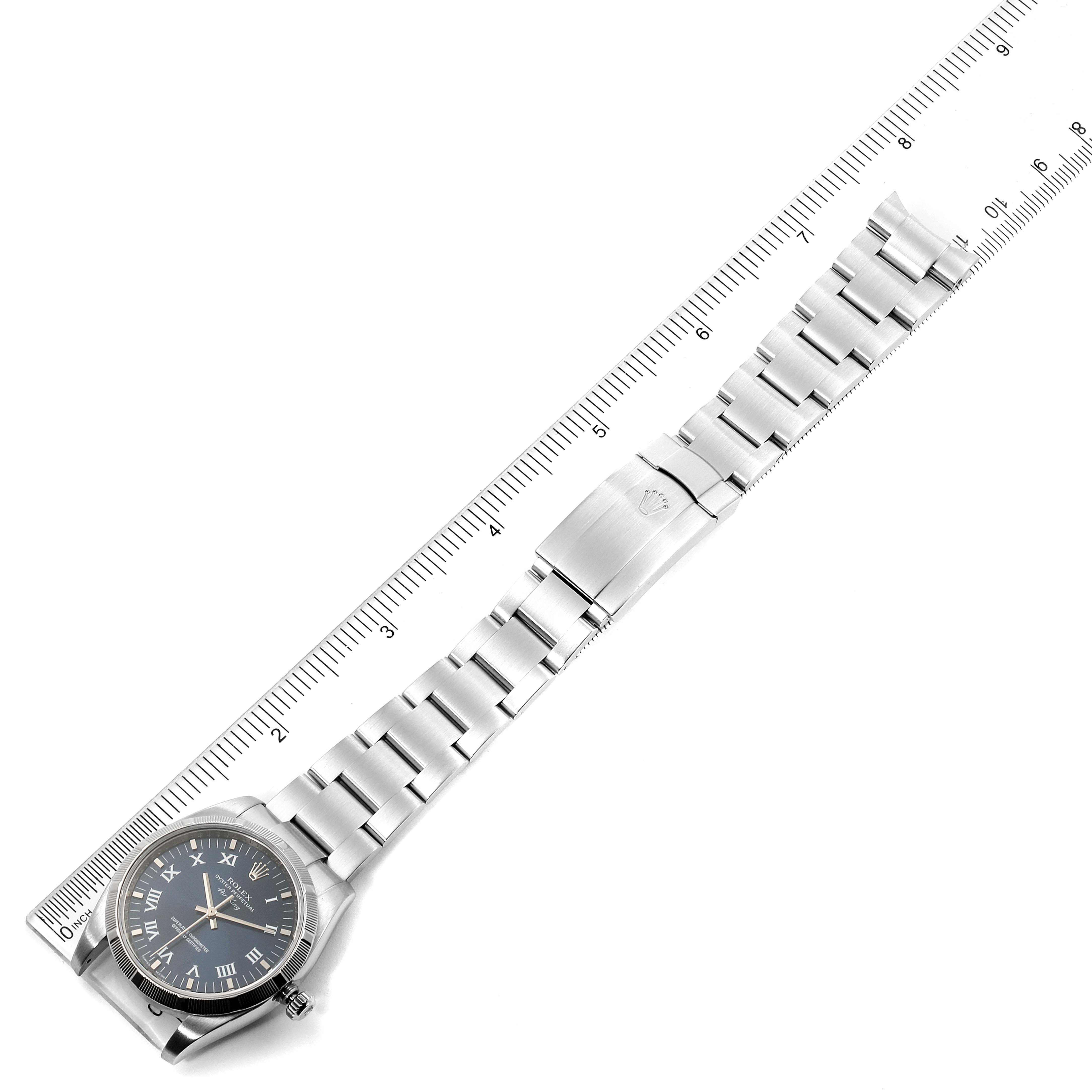 This image shows an overhead view of a Rolex Air-King 114210 Men's Stainless Steel Blue Dial 114210 Men's Stainless Steel Blue Dial watch, displaying its face, bracelet, and clasp beside a ruler for scale.