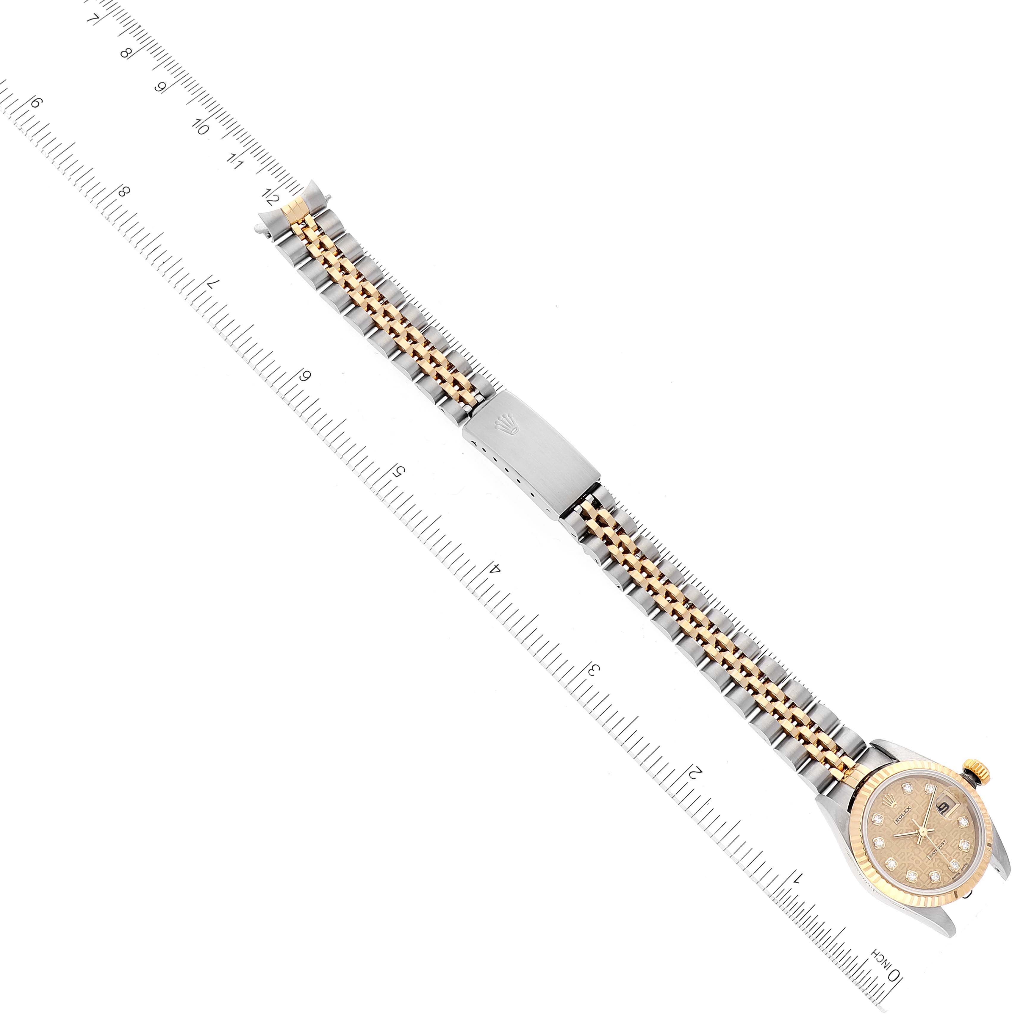 The Rolex Datejust 79173 Women's Steel and Gold (two tone) Champagne Dial 79173 Women's Steel and Gold (two tone) Champagne Dial watch is shown from a top-down angle, featuring its face, bezel, bracelet, and clasp on a ruler.
