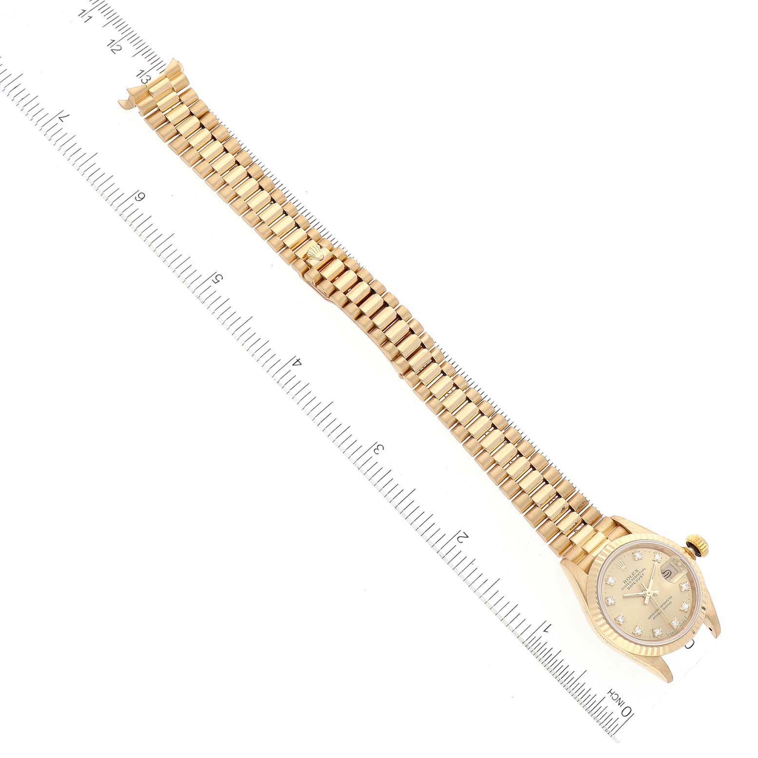 The Rolex President 69178 Women
s Yellow Gold Champagne Dial 69178 Women
s Yellow Gold Champagne Dial model watch is shown flat with its gold band fully extended, placed next to a measuring ruler for scale.