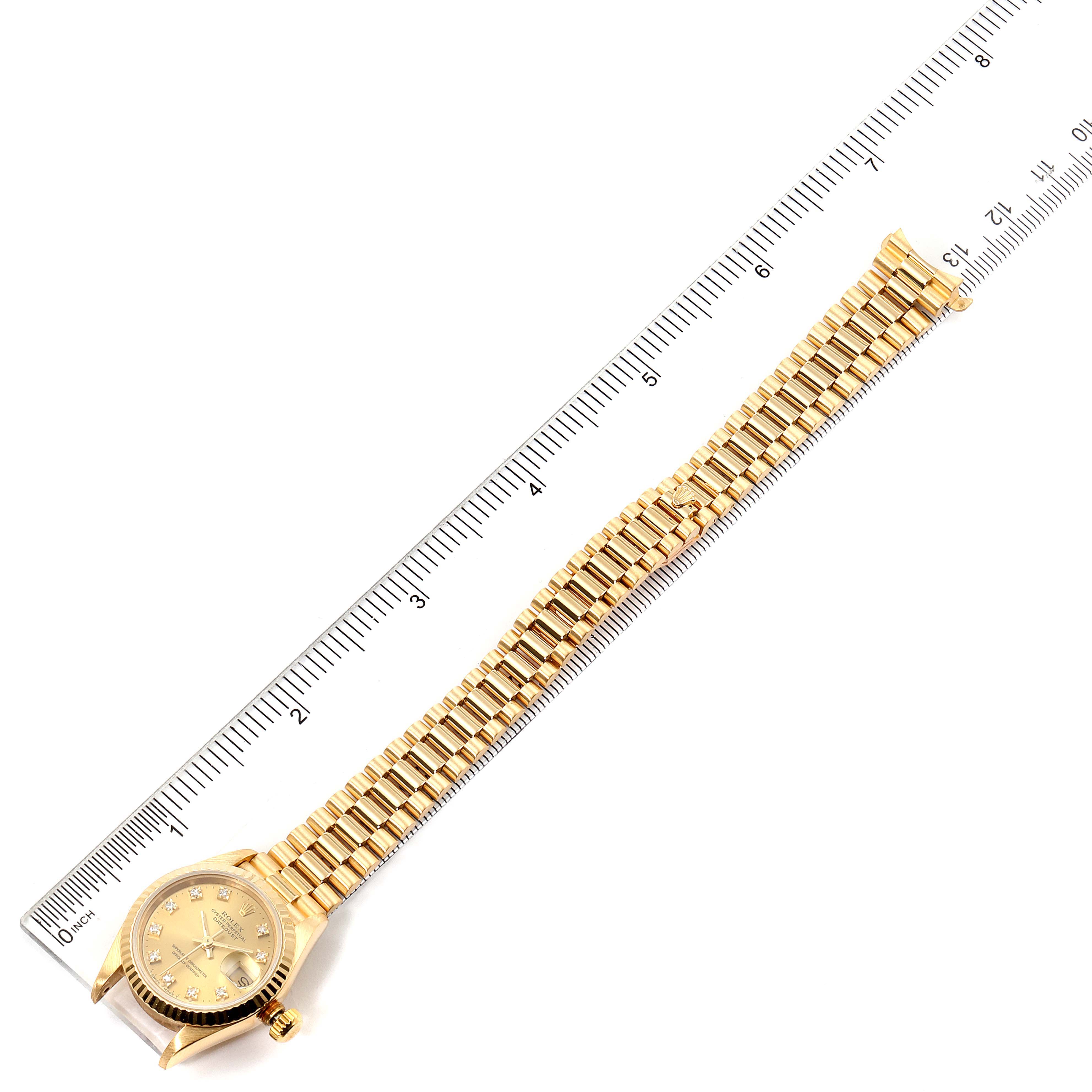 The image shows a top view of a Rolex President 69178 Women
s Yellow Gold Champagne Dial 69178 Women
s Yellow Gold Champagne Dial watch with its gold bracelet laid out next to a ruler.