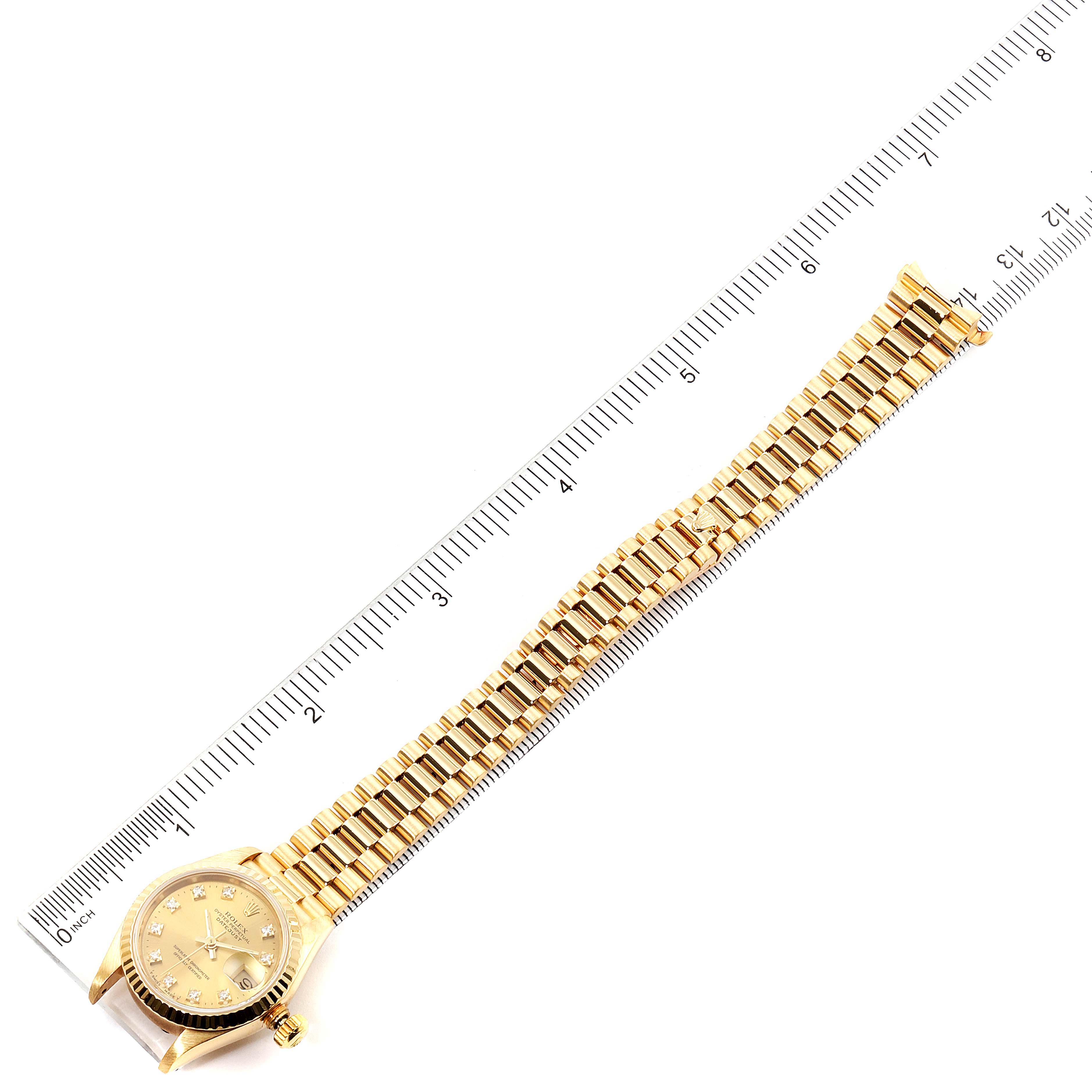 The image shows a top-down view of a Rolex President 69178 Women
s Yellow Gold Champagne Dial 69178 Women
s Yellow Gold Champagne Dial model watch with its band extended alongside a ruler.