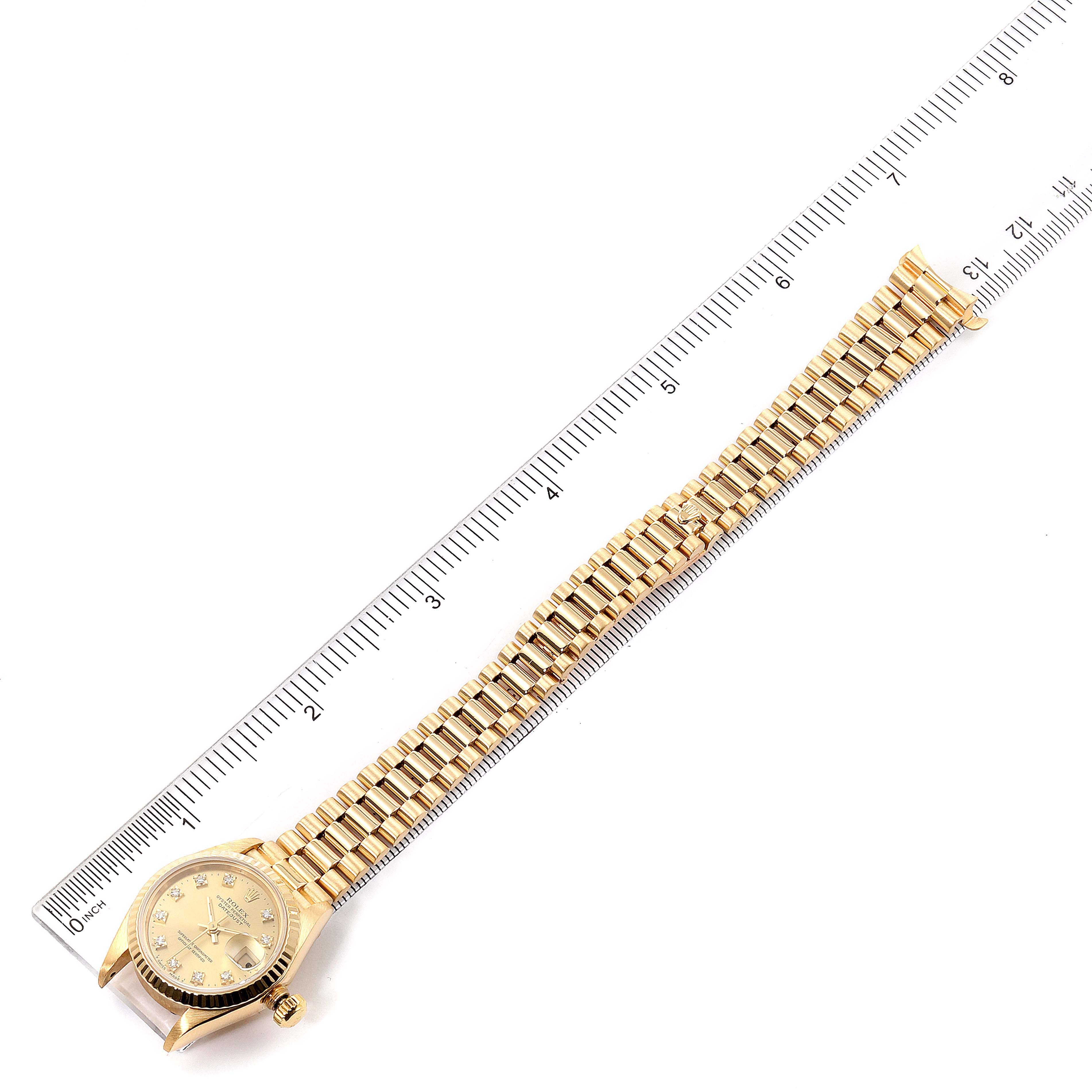 The image shows a Rolex President 69178 Women
s Yellow Gold Champagne Dial 69178 Women
s Yellow Gold Champagne Dial watch laid flat next to a ruler, displaying its bracelet and face from a top-down angle.