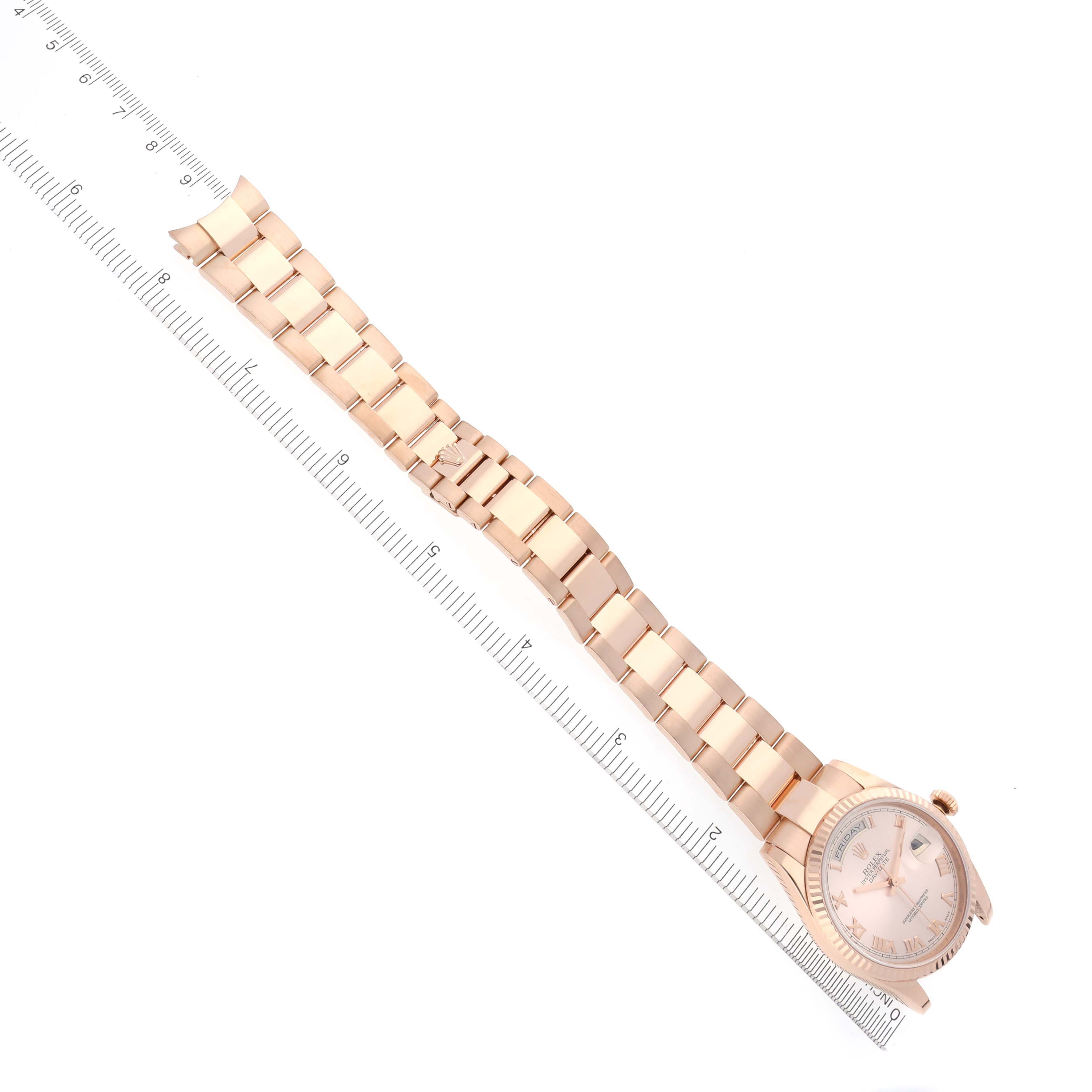 The Rolex President 118235 Men
s Rose Gold Pink Dial 118235 Men
s Rose Gold Pink Dial model watch is shown from an angled top view, displaying the face, case, and bracelet alongside a ruler.