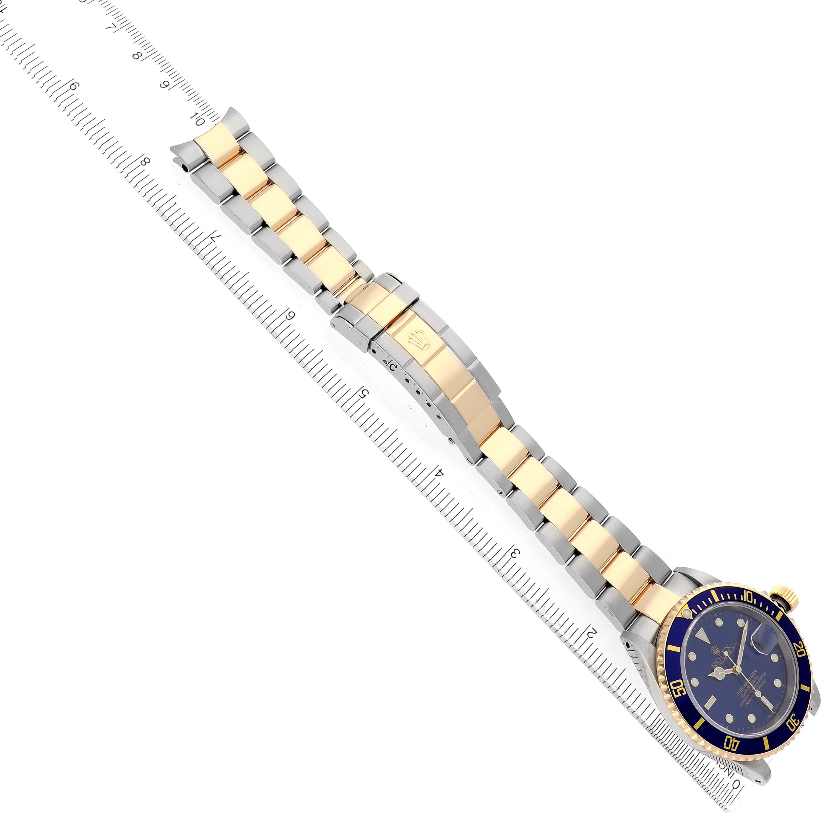 The Rolex Submariner 16613 Men's Steel and Gold (two tone) Blue Dial watch is shown from a top view, displaying the bracelet and clasp alongside a ruler.
