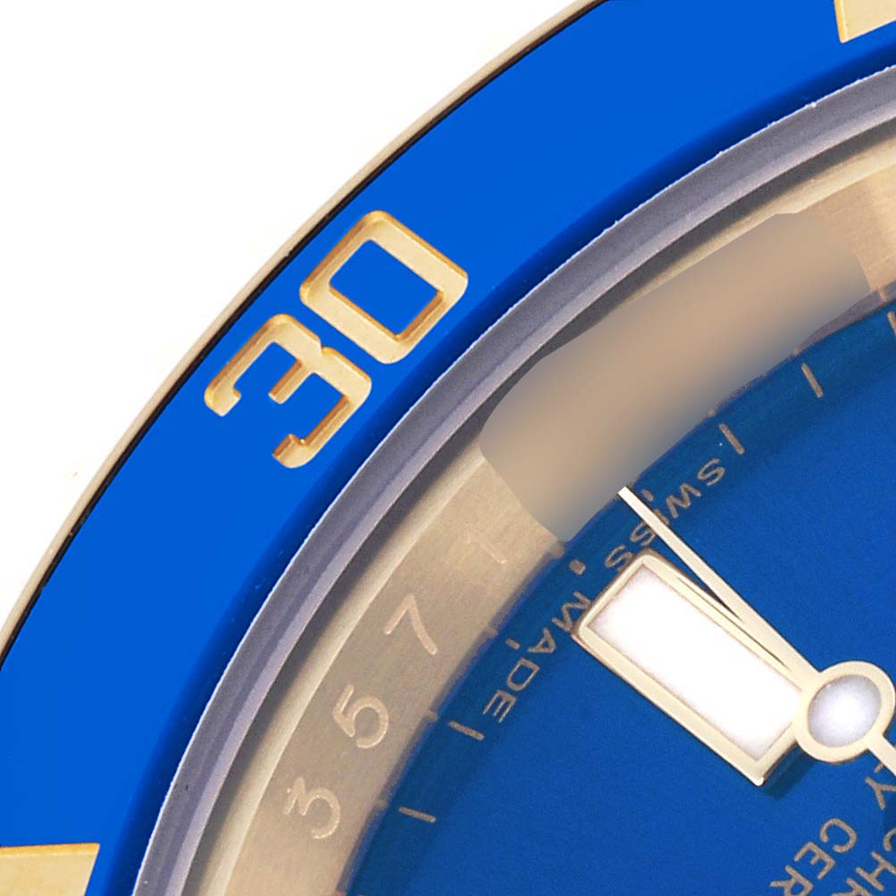 The image shows a close-up of the Rolex Submariner 116618LB Men's Yellow Gold Blue Dial 116618LB Men's Yellow Gold Blue Dial's blue bezel with gold numerals and a portion of the watch face and hands.