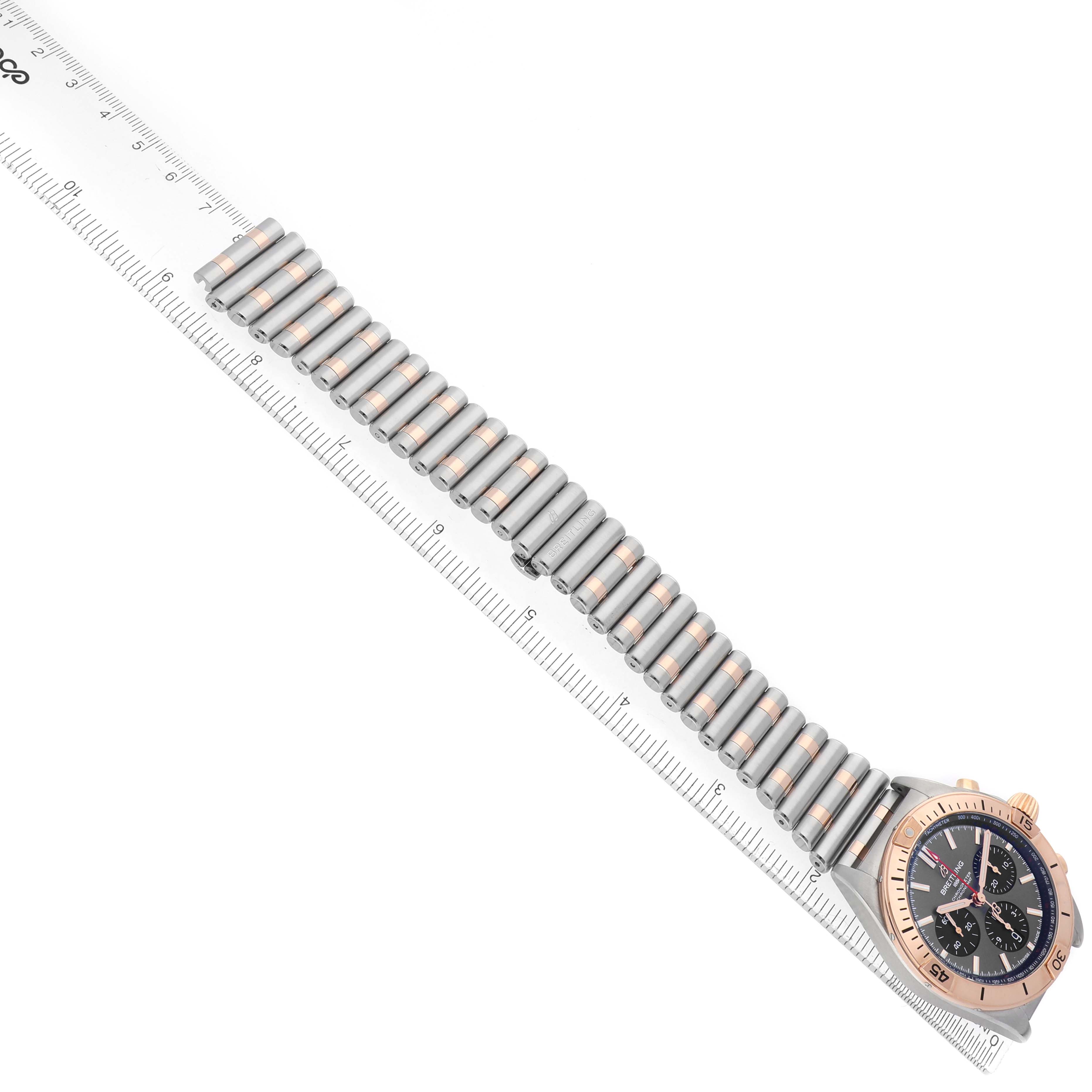 The Breitling Chronomat UB0134 Men's Steel and Gold (two tone) Grey Dial watch is shown diagonally with a focus on its band, case, and bezel alongside a ruler for scale.