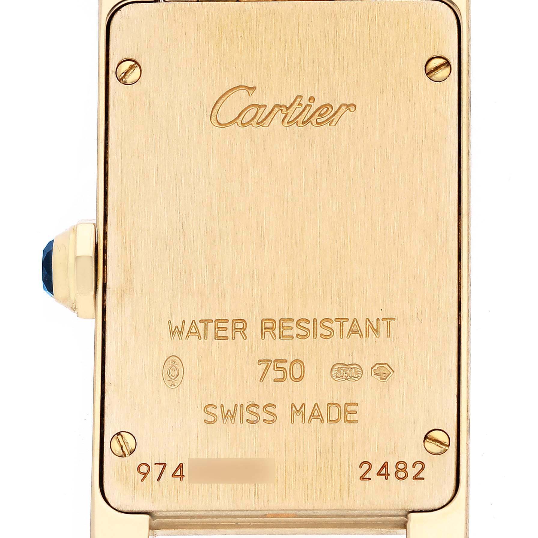 The image shows the back of a Cartier Tank Americaine W26015K2 Women's Yellow Gold Silver Dial watch, featuring engravings and side view of the crown with a blue gemstone.