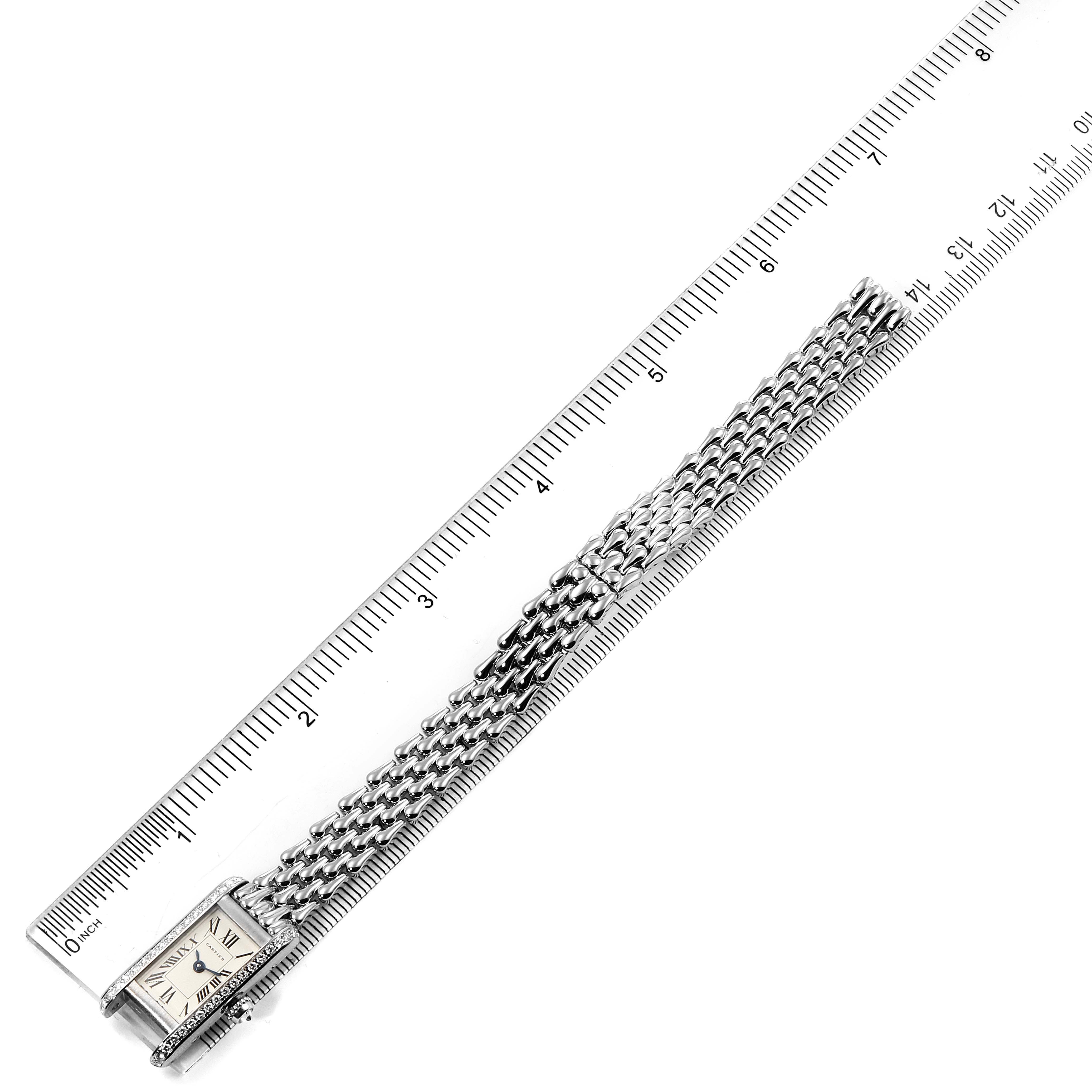 The image shows a Cartier Tank Américaine watch laid flat with its face, bracelet, and ruler for scale.