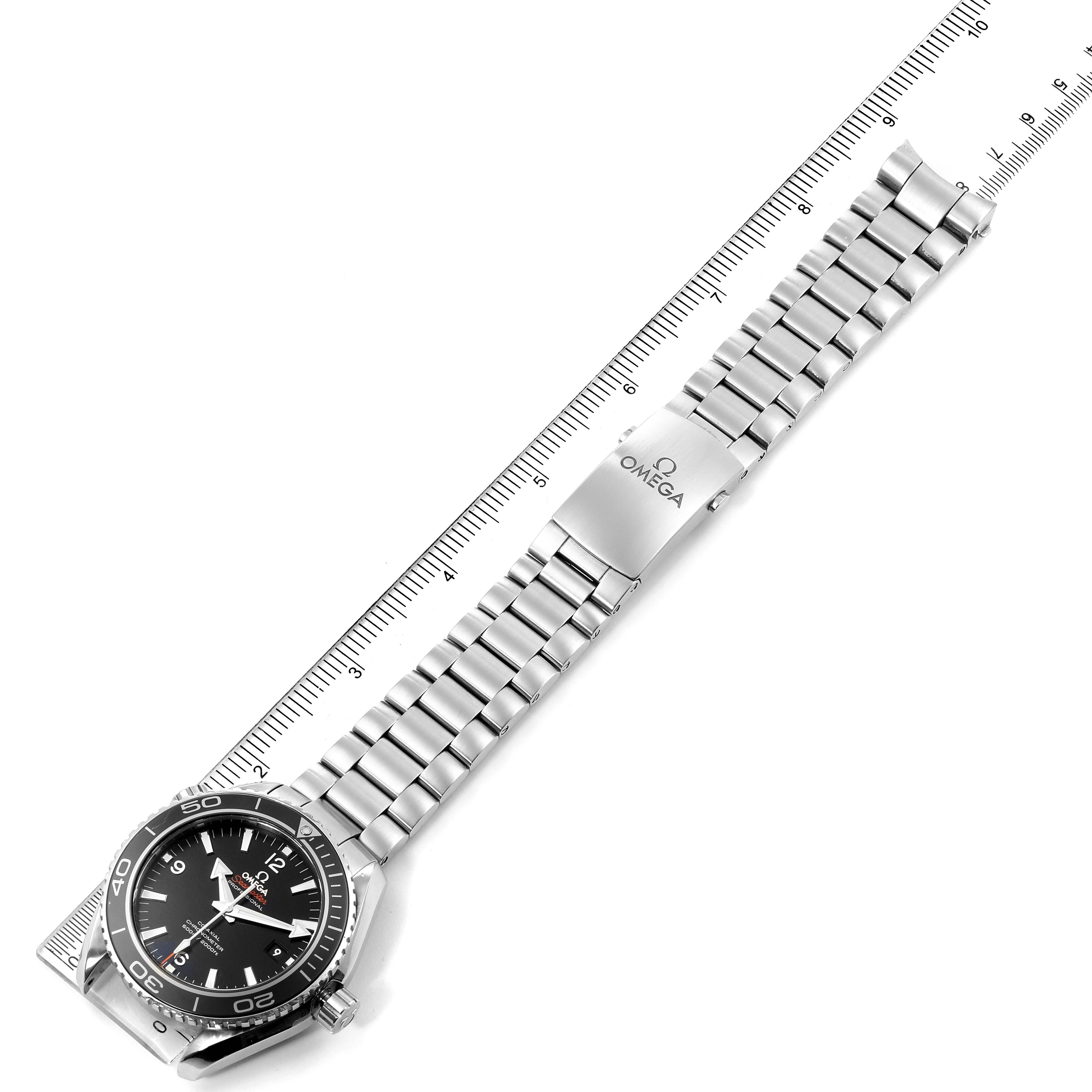 The image shows an Omega Planet Ocean 232.30.46.21.01.001 Men
s Stainless Steel Black Dial 232.30.46.21.01.001 Men
s Stainless Steel Black Dial watch laid flat with its stainless steel bracelet extended, alongside a ruler for measurement.