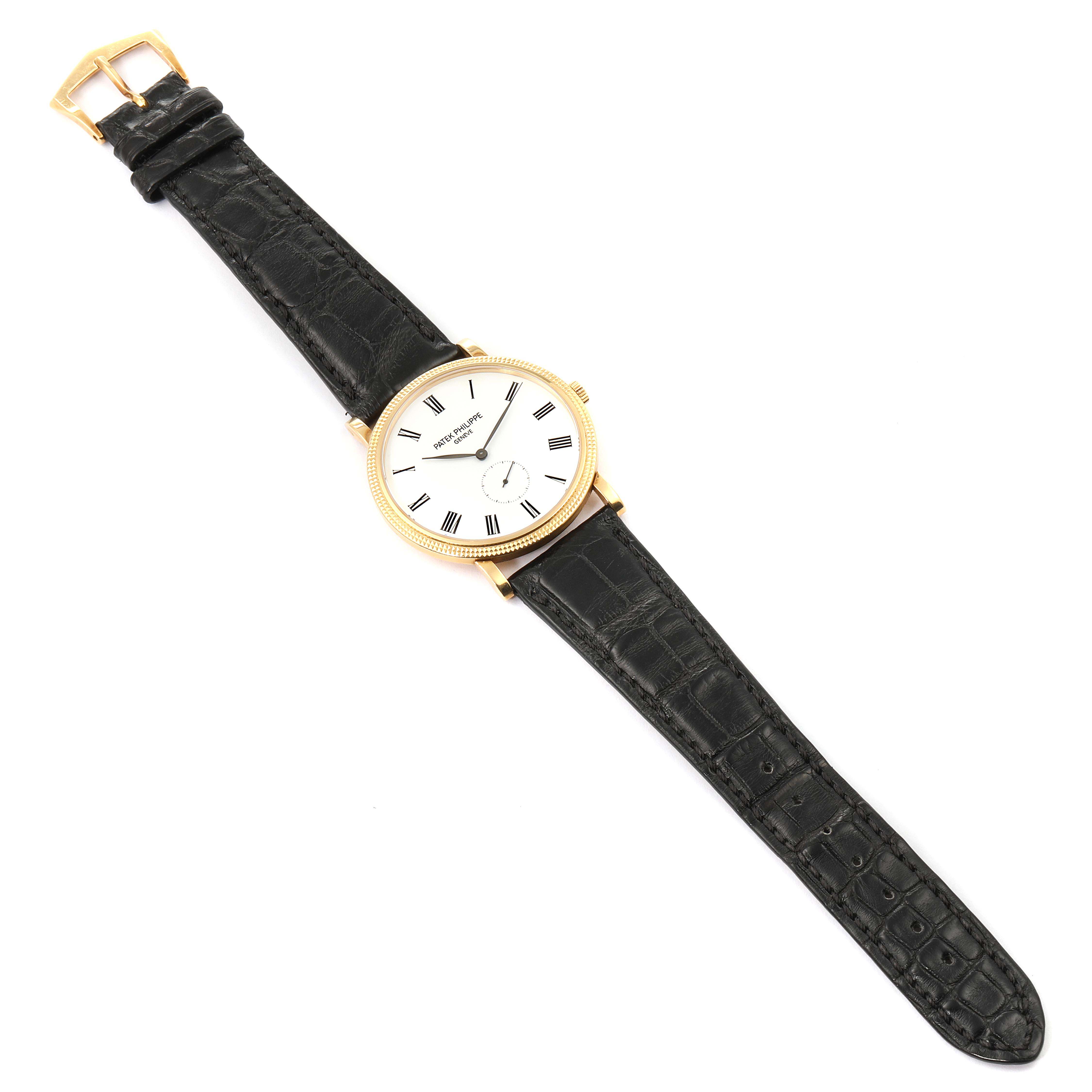 The image shows a top-down view of a Patek Philippe Calatrava 5119J Men's Yellow Gold White Dial 5119J Men's Yellow Gold White Dial watch with a black leather strap and a gold case.